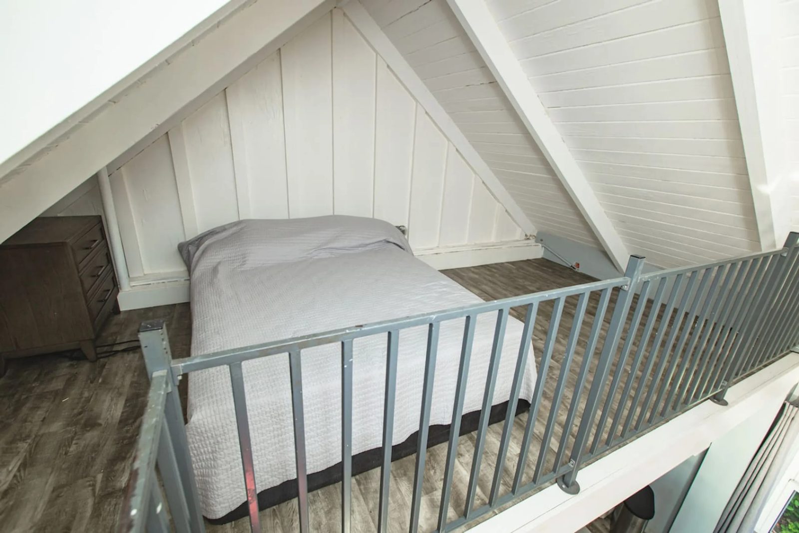 A single bed in the loft of The Cerulean's guest cottage under a pitched white ceiling, behind a metal railing