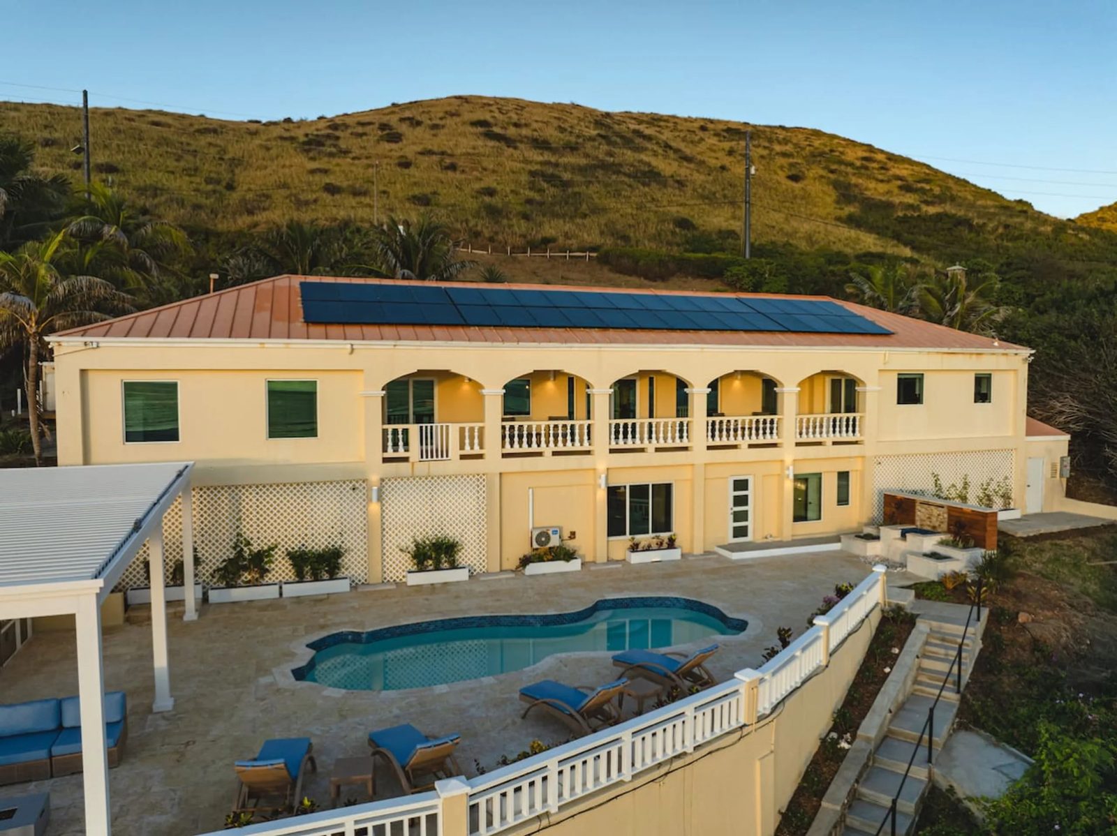 The Cerulean villa on St. Croix, a two-storey pale yellow house with an arched upper veranda, a pool deck below and steps with a handrail leading down the slope