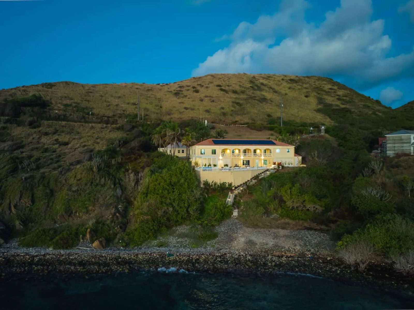 Aerial view from the sea of The Cerulean on a green hillside on St. Croix, with a long stepped path running down to a stony shoreline