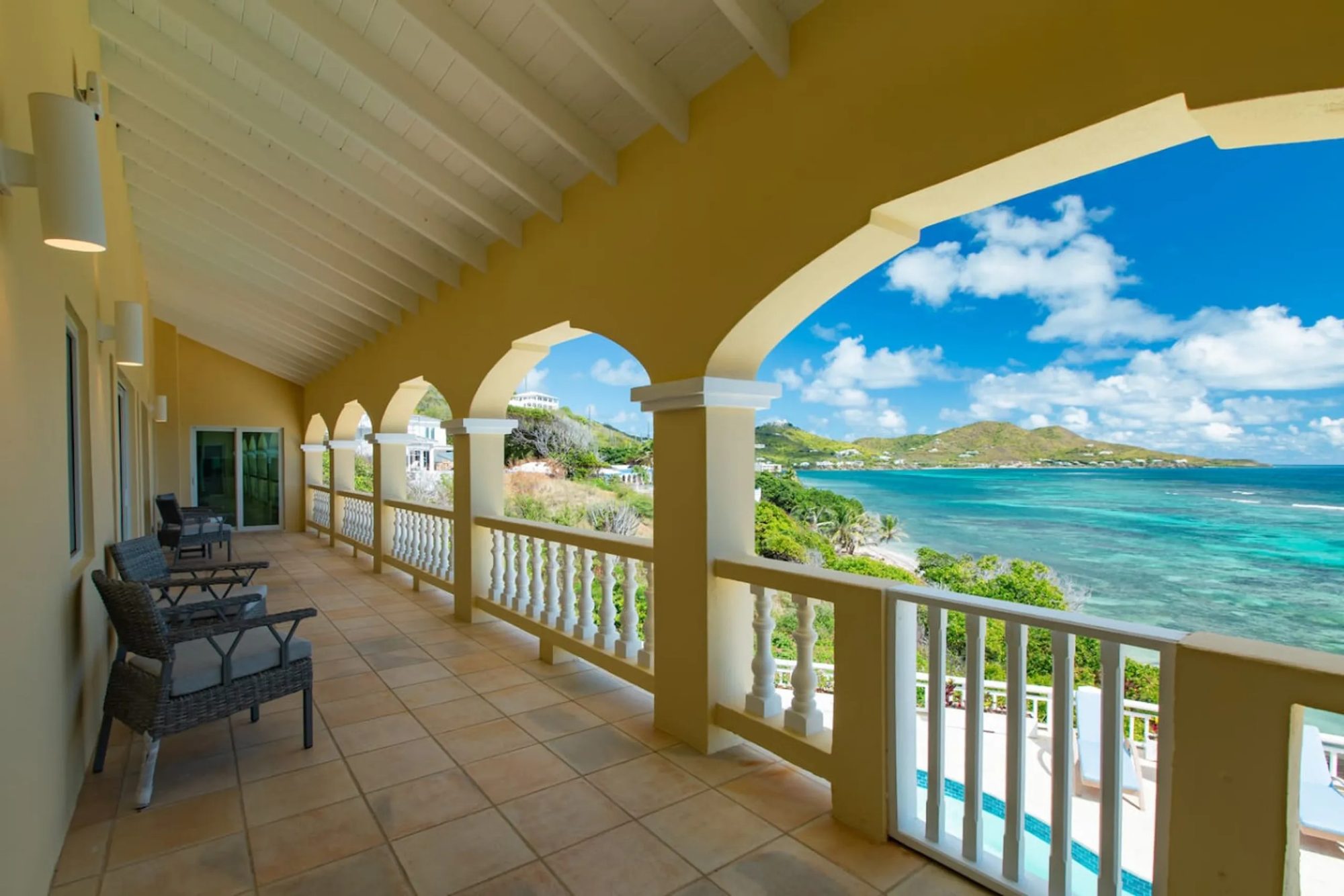 The arched veranda of The Cerulean villa on St. Croix, with cream columns and balustrades framing a turquoise bay and a green headland