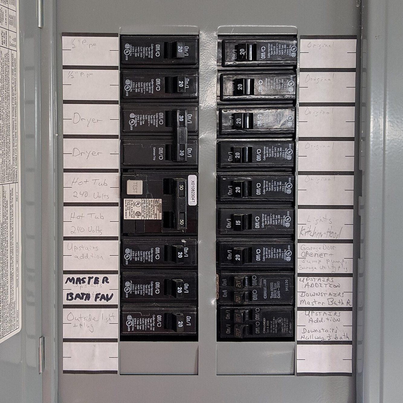 An open electrical breaker panel with two rows of black breakers, each labelled by hand on paper strips: dryer, hot tub, master bath fan, outside light and plug, kitchen hood lights