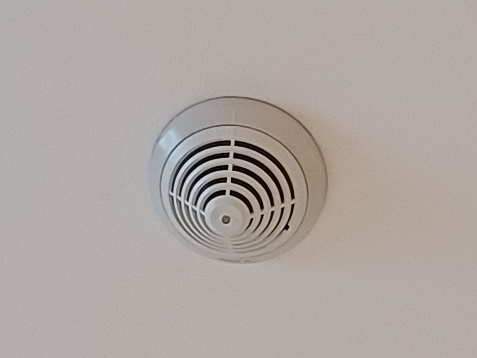 A round white smoke detector mounted in the middle of a plain white ceiling