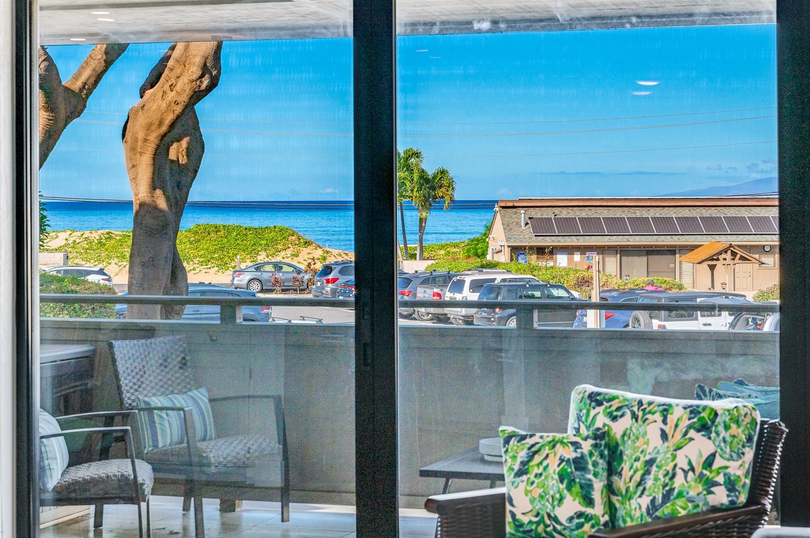 The view from the Modern Ocean View through its sliding doors, past the lanai chairs and a car park, to vine-covered dunes, palm trees and the sea