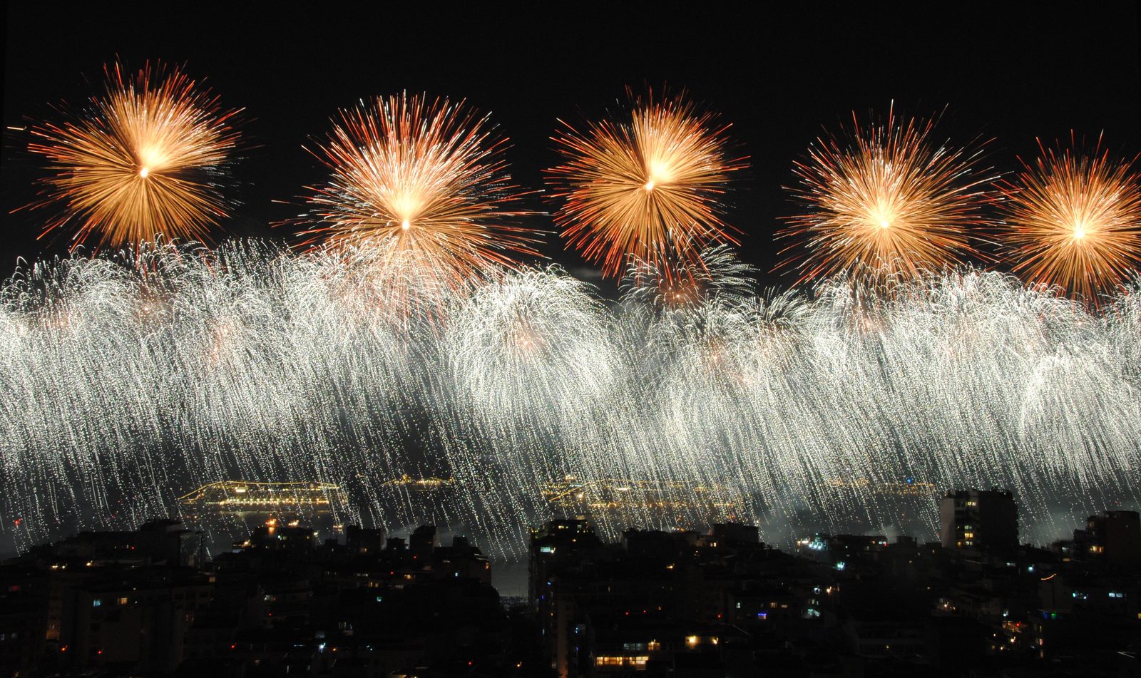 Fireworks burst in gold and white over the sea off Copacabana on New Year's Eve, above lit cruise ships offshore and the dark apartment blocks of the neighbourhood