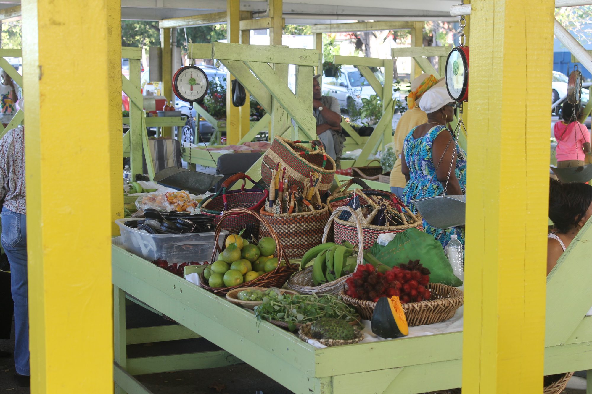 Plantains, citrus, a soursop, herbs and woven baskets on a stall at a farmers' market on St. Croix, with hanging scales above