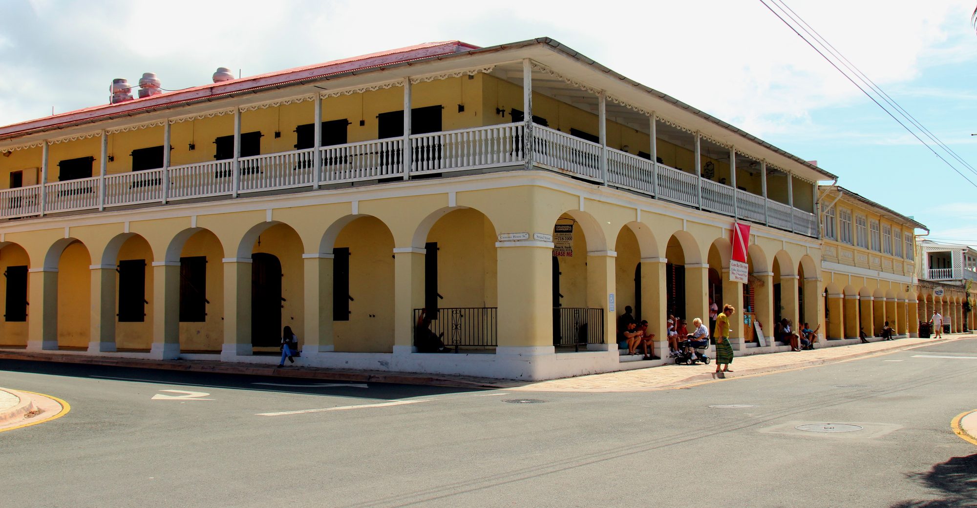 A pale yellow arcaded building with a white wooden upper gallery at a street corner in Frederiksted on St. Croix