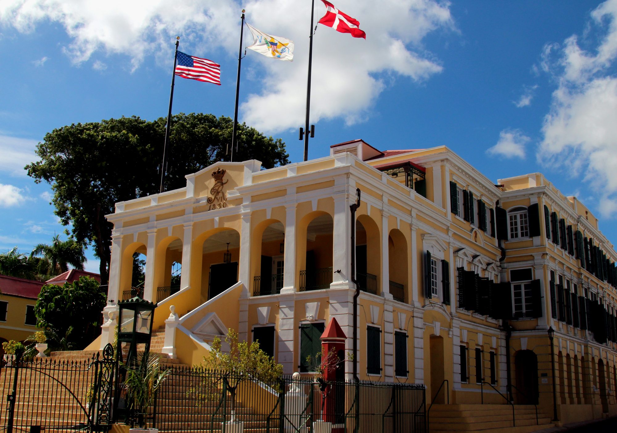 Government House in Christiansted on St. Croix, a pale yellow building with a double entrance stair, with the U.S., Virgin Islands and Danish flags flying above it