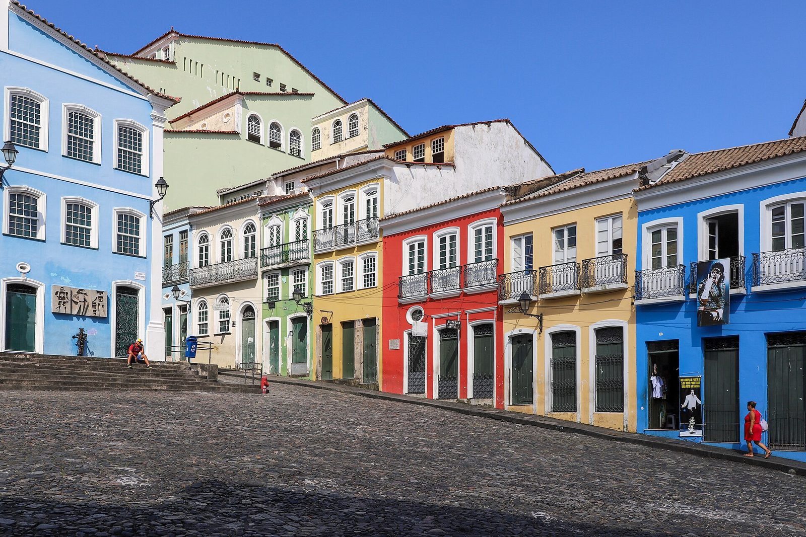 The sloping cobbled Largo do Pelourinho in Salvador, lined with two-storey colonial houses painted blue, cream, green, yellow and red, with white window frames and iron balconies
