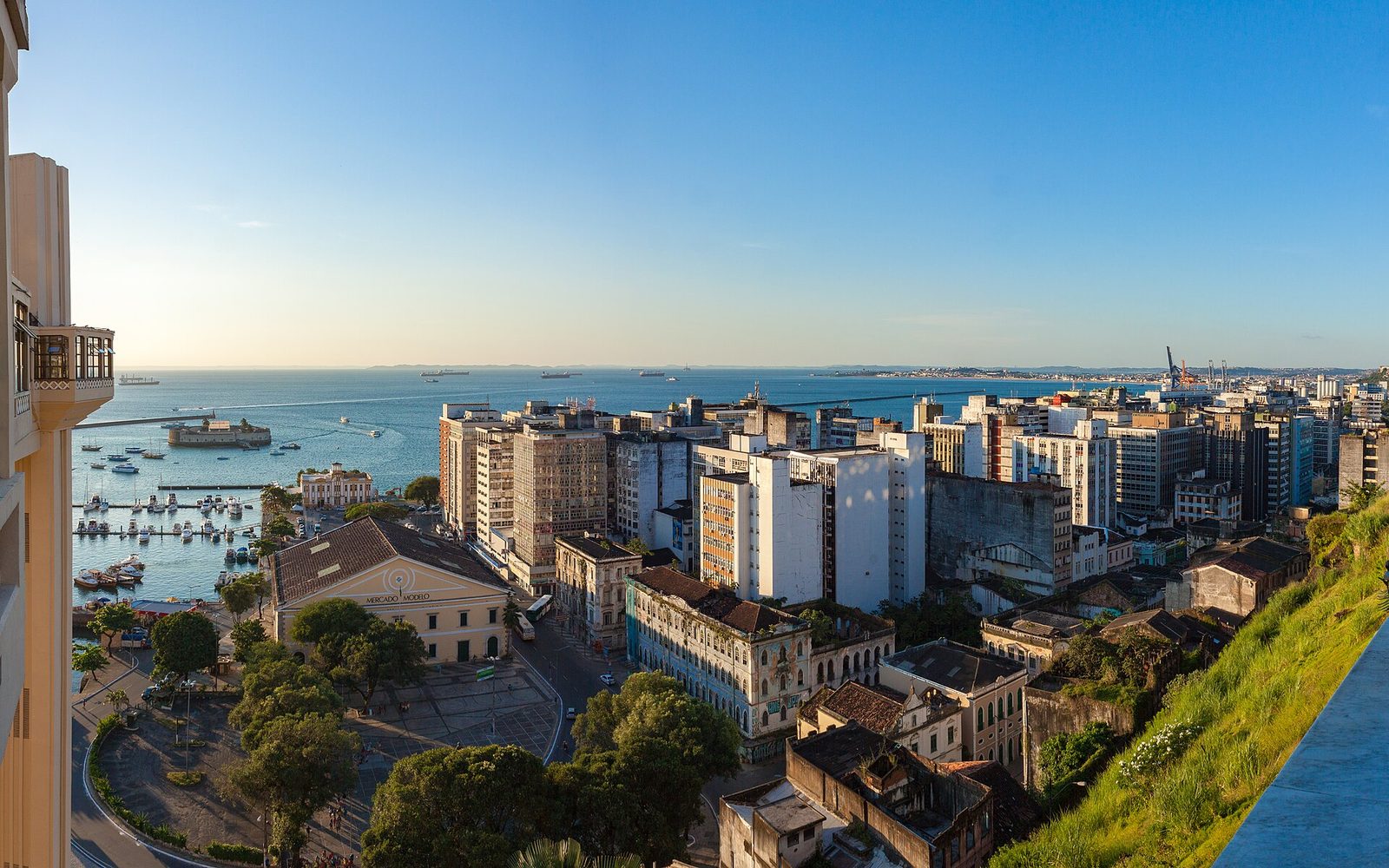View from the upper town over the yellow Mercado Modelo building, a marina crowded with small boats, a round fort in the water, the office blocks of the lower town and ships anchored in the Bay of All Saints