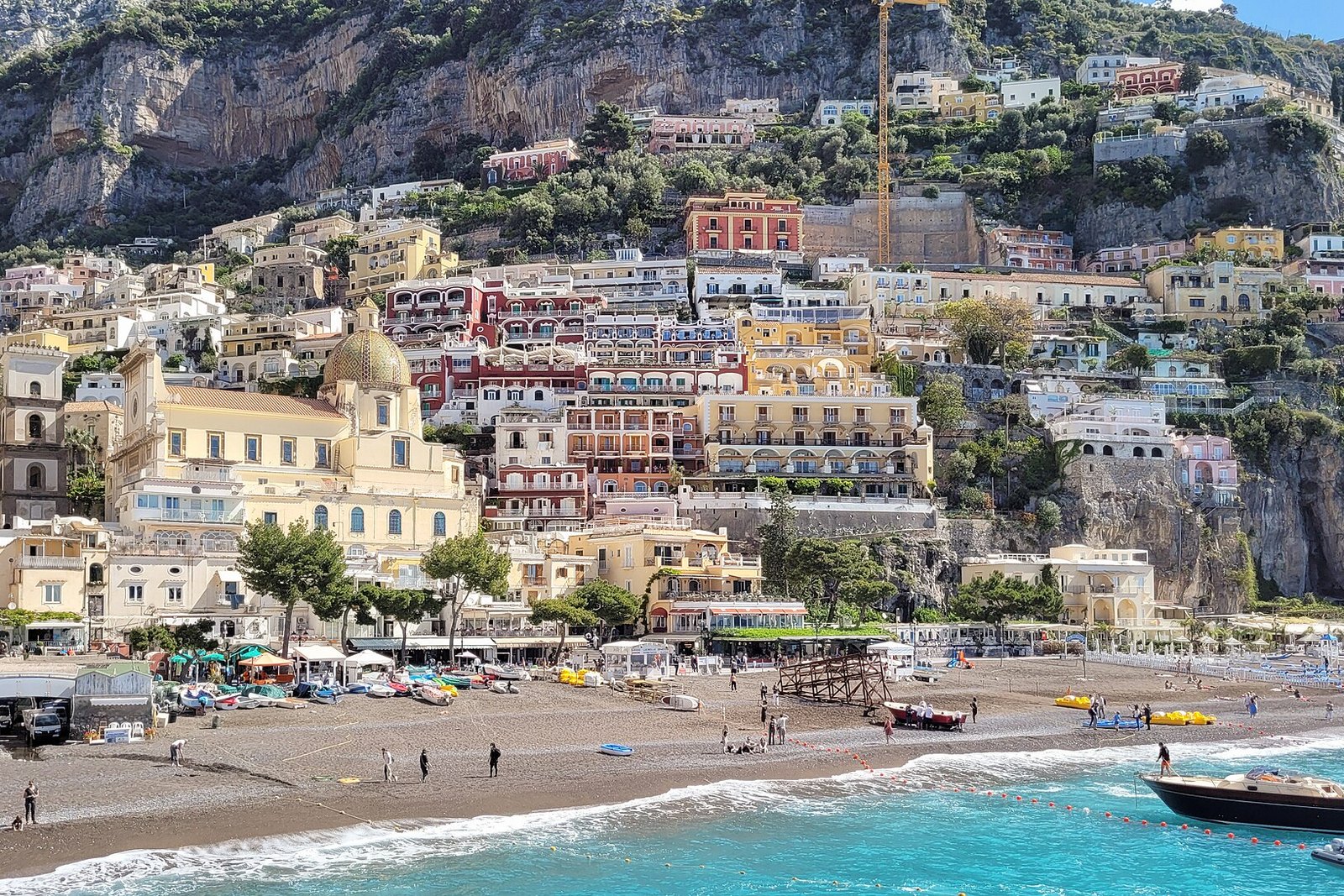 A pebbly beach with parasols, boats and swimmers below Positano’s pastel houses climbing the steep cliffs behind, with a domed church at the centre