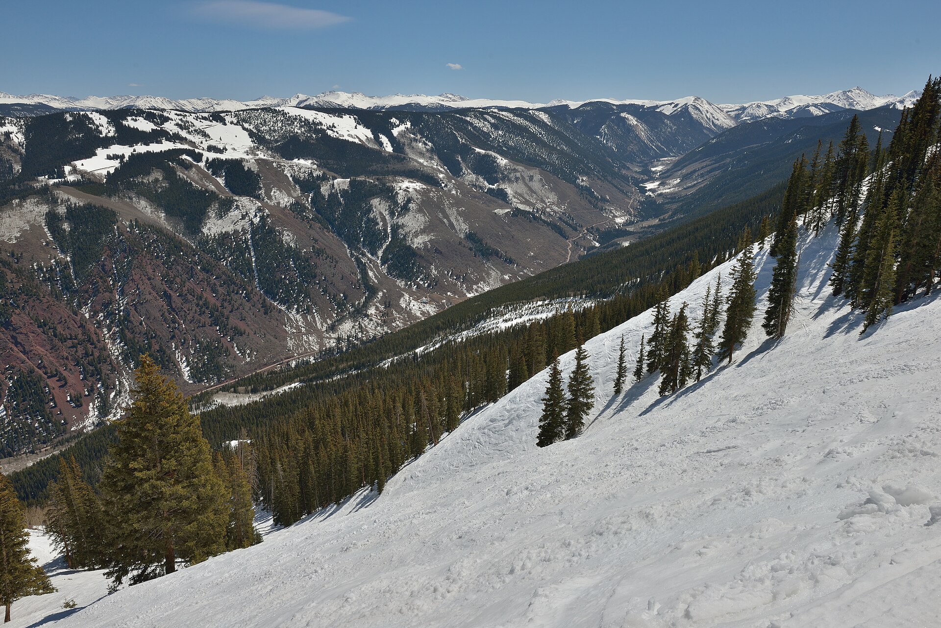 Skiers on a wide groomed run at Snowmass with the Colorado high country beyond