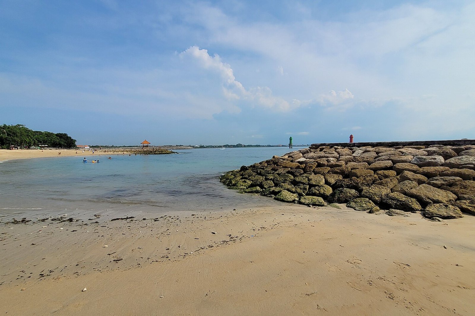 A sandy beach at Sanur on Bali with a rock breakwater running into calm water under a pale sky