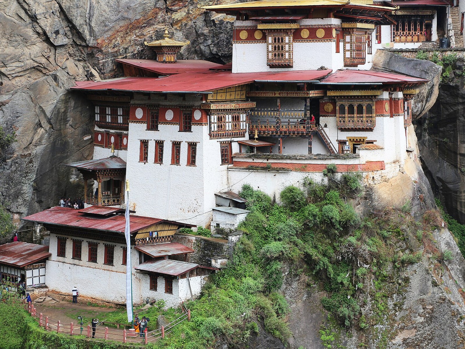 Taktsang Monastery, white buildings with red roofs built against a sheer cliff face above a forested slope in Bhutan
