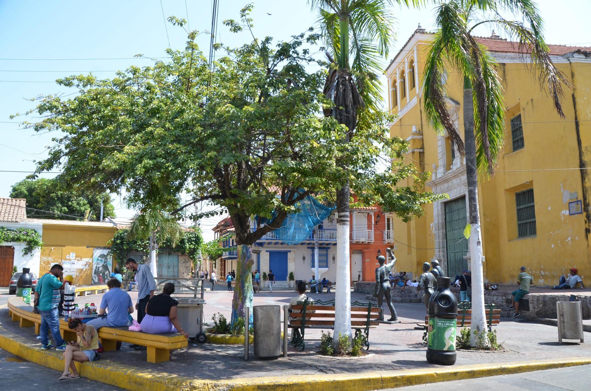 A small plaza in the Getsemaní barrio with a pale colonial church, painted low houses and strings of coloured flags overhead.
