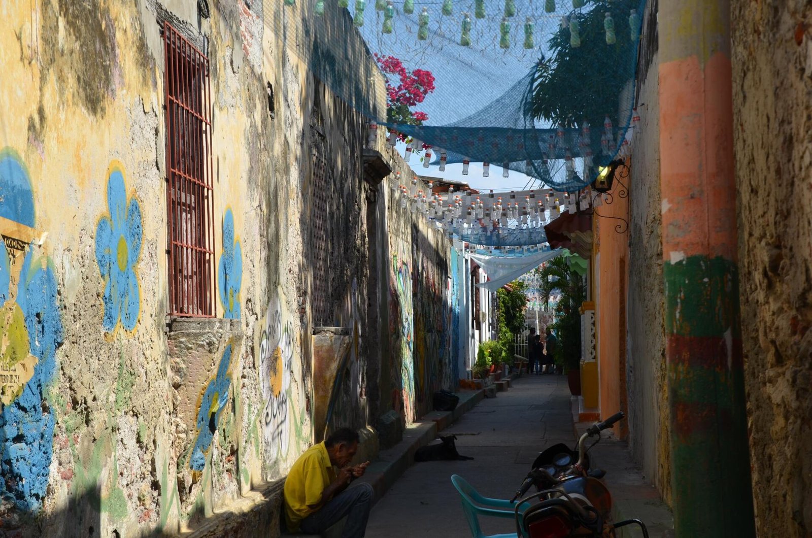 A street corner in Cartagena with a cream-coloured building featuring two wooden balconies with flowers, and a street extending left with colourful buildings and pedestrians.