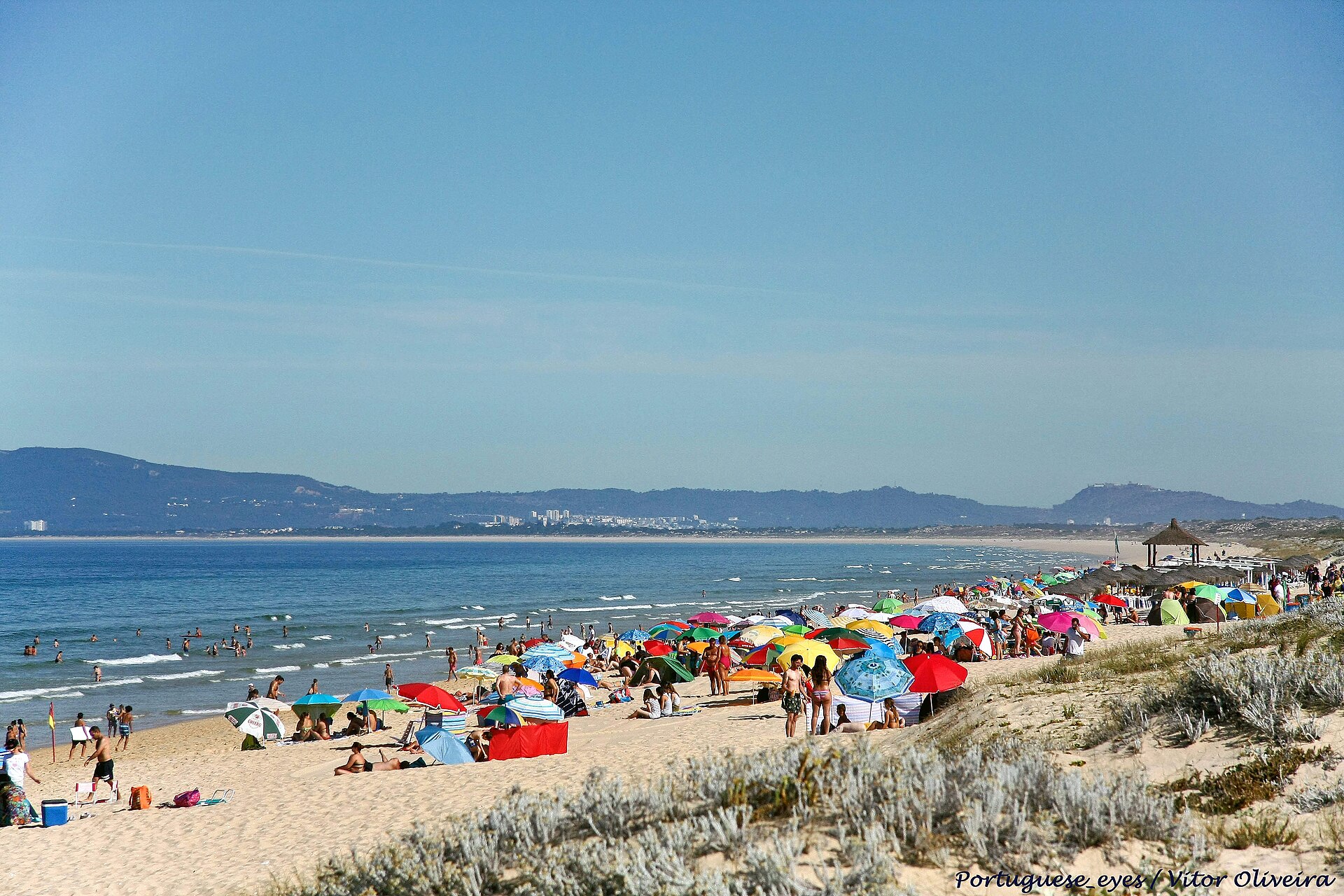A wide, near-empty stretch of Praia da Comporta with dunes and a boardwalk under a clear sky