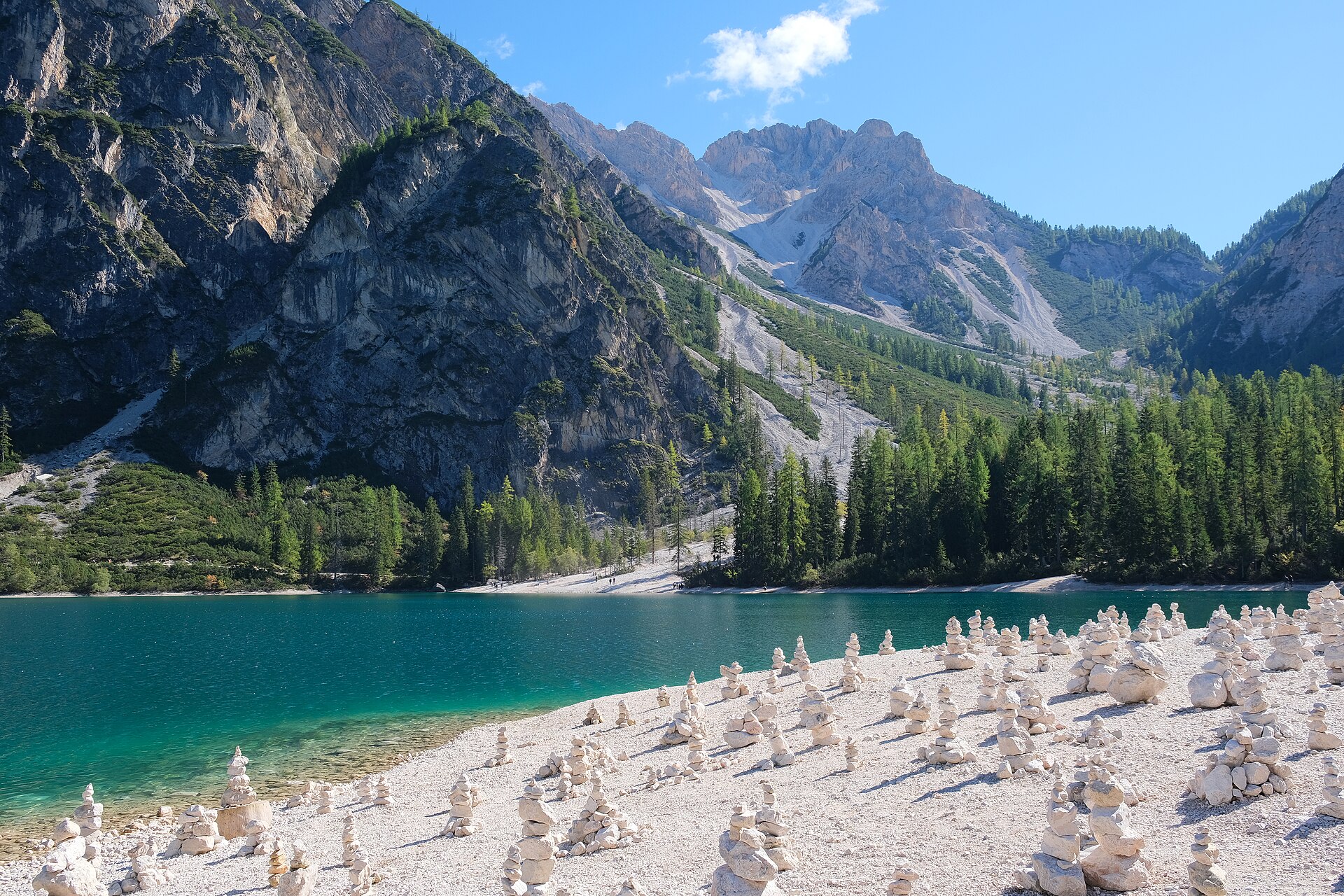 A still turquoise lake ringed by pine forest with a wooden boathouse and a steep peak rising behind.