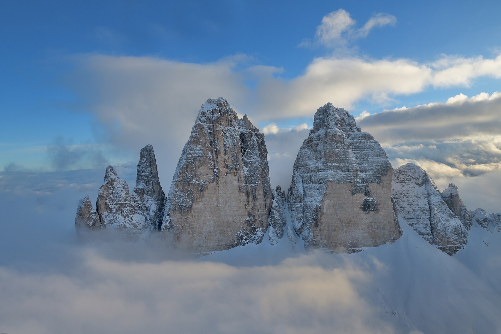 Three sheer parallel rock peaks rising from grey scree slopes under a clear morning sky.