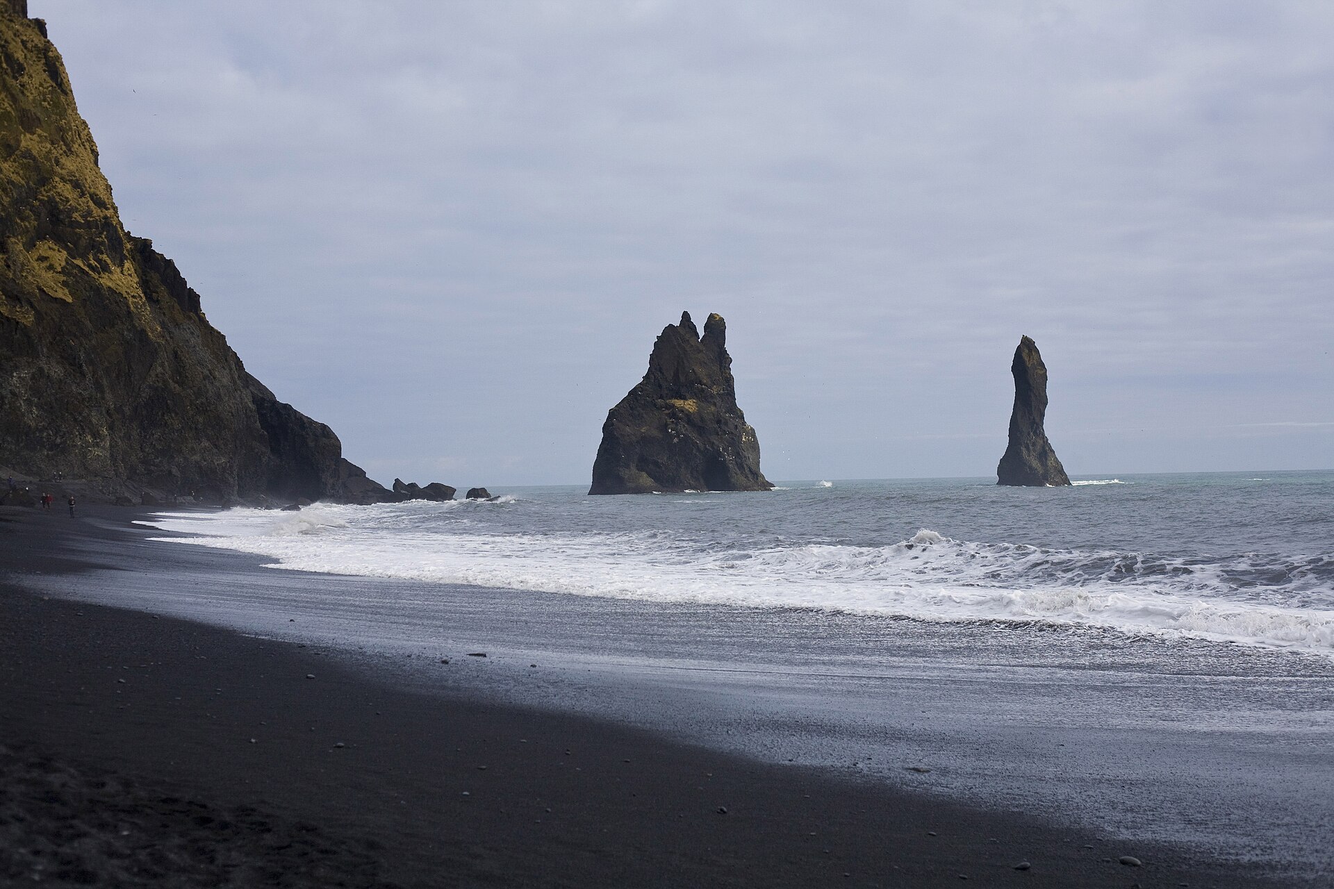 Black volcanic sand and columns of hexagonal basalt rising at the edge of a grey ocean.