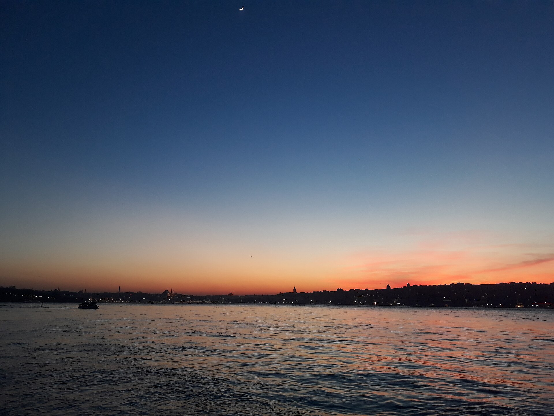 A passenger ferry crossing the Bosphorus strait with the domes and minarets of Istanbul's old city on the far shore.