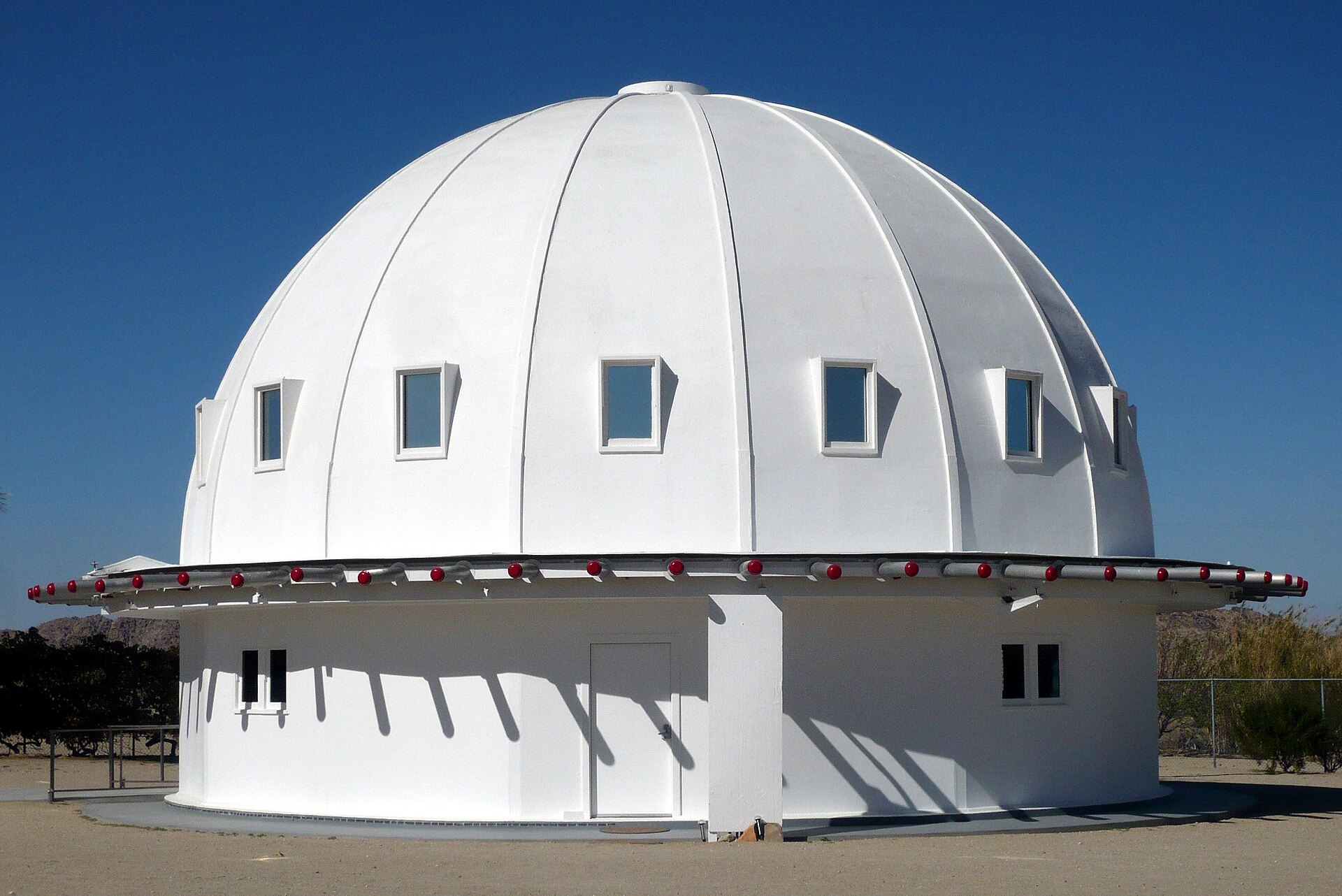 The white domed Integratron with a ring of small windows and a red-lit rim, standing alone in the desert at Landers, California, under a deep blue sky