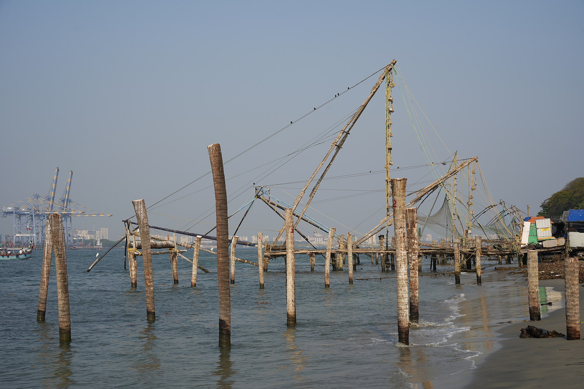 Cantilevered Chinese fishing nets on wooden frames along the shore at Fort Kochi at low tide.