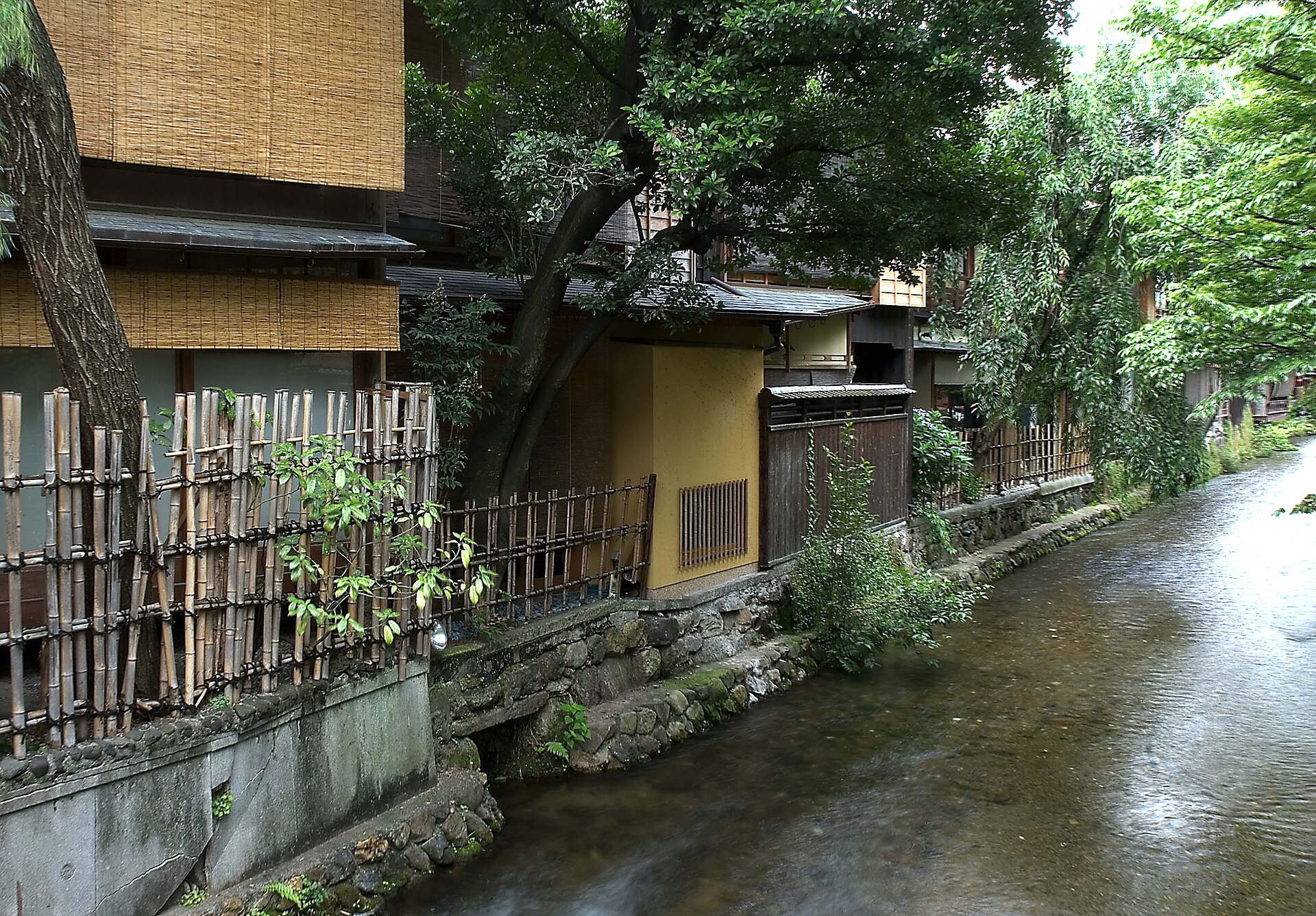 A quiet canal lined with willow trees and wooden townhouses in the Gion district of Kyoto.