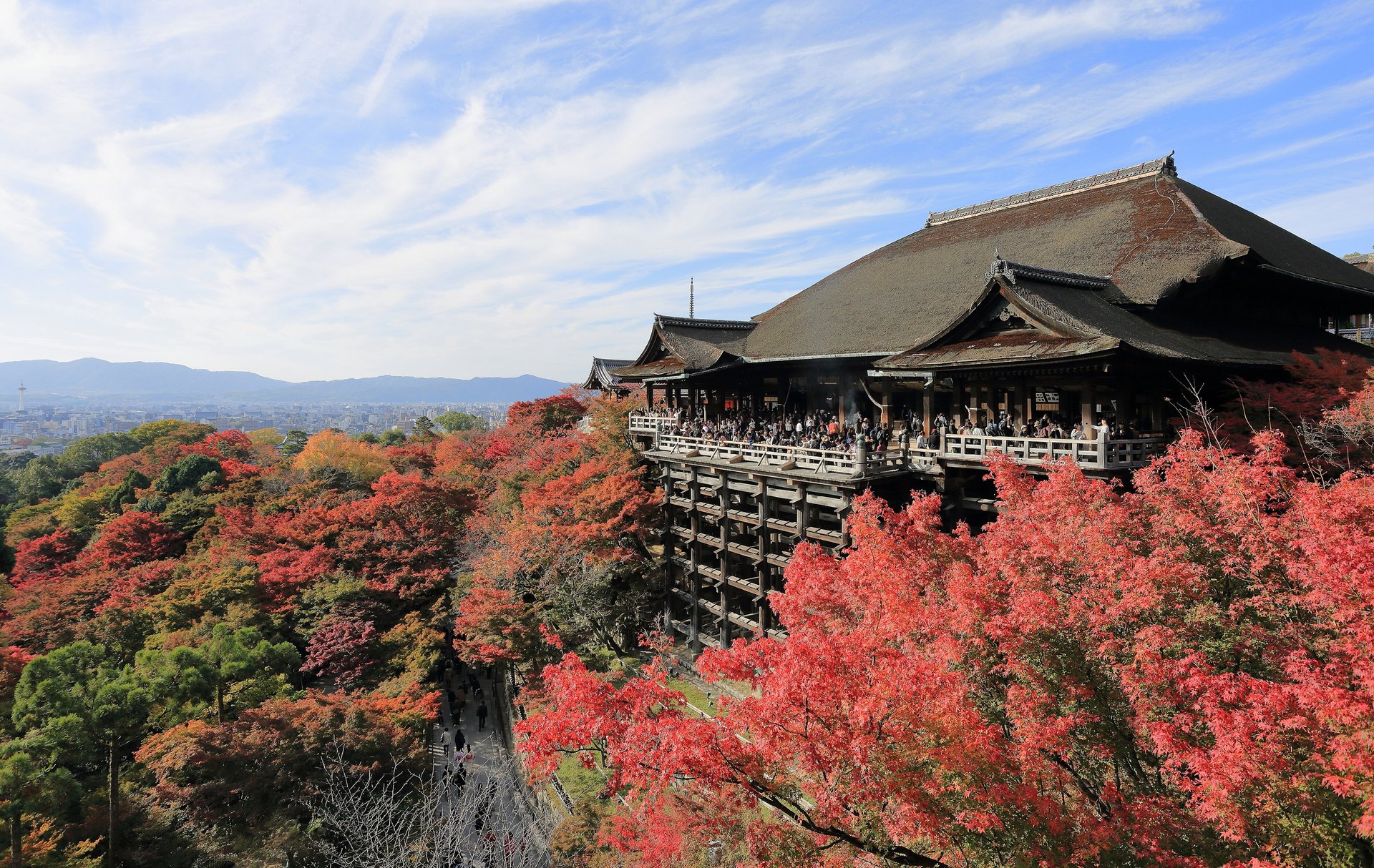 The wooden stage of Kiyomizu-dera temple among red and orange maple trees in autumn, with the city of Kyoto spread out beyond