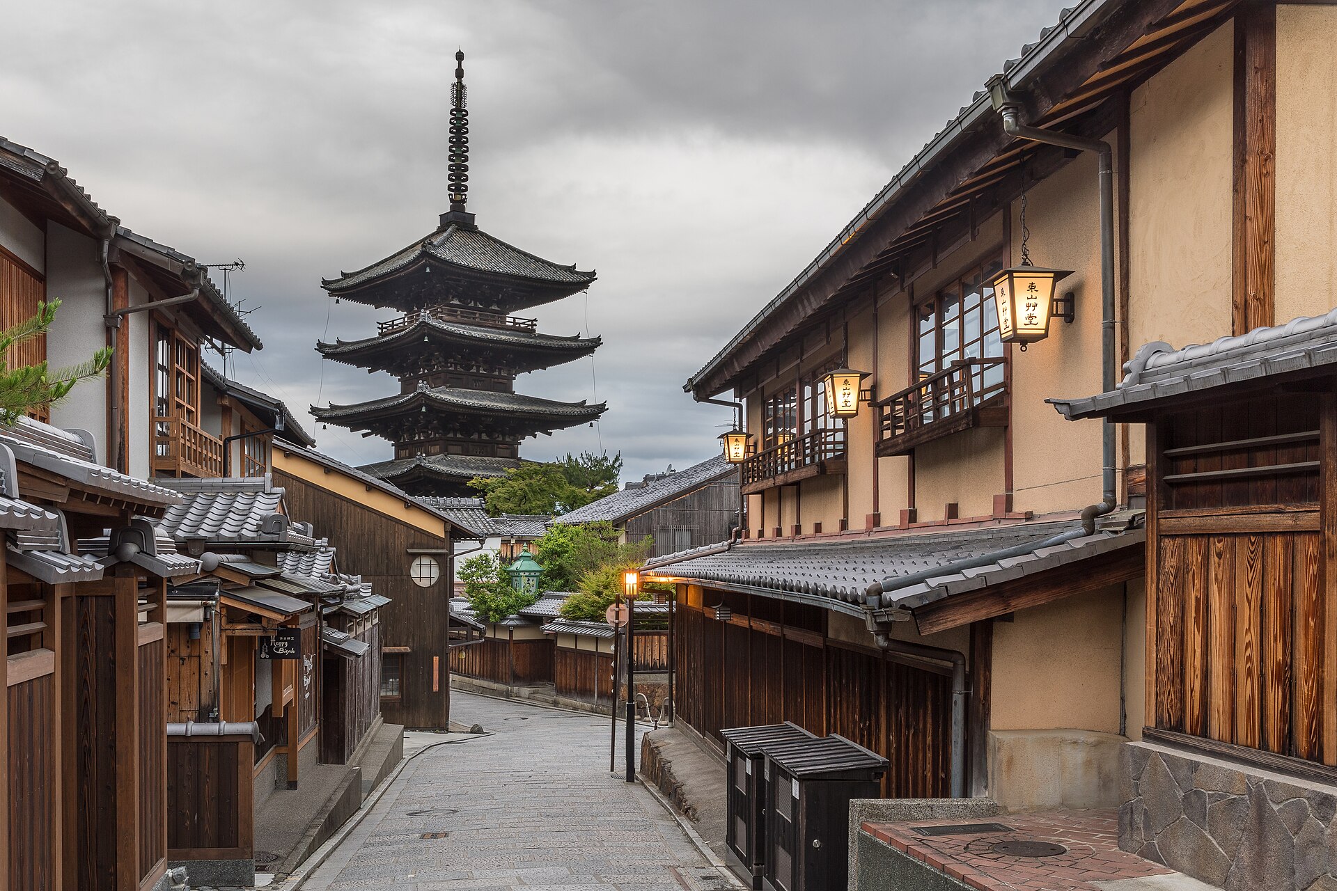 The Yasaka Pagoda rising above a sloping street of wooden machiya houses in Kyoto's Higashiyama district at dusk.