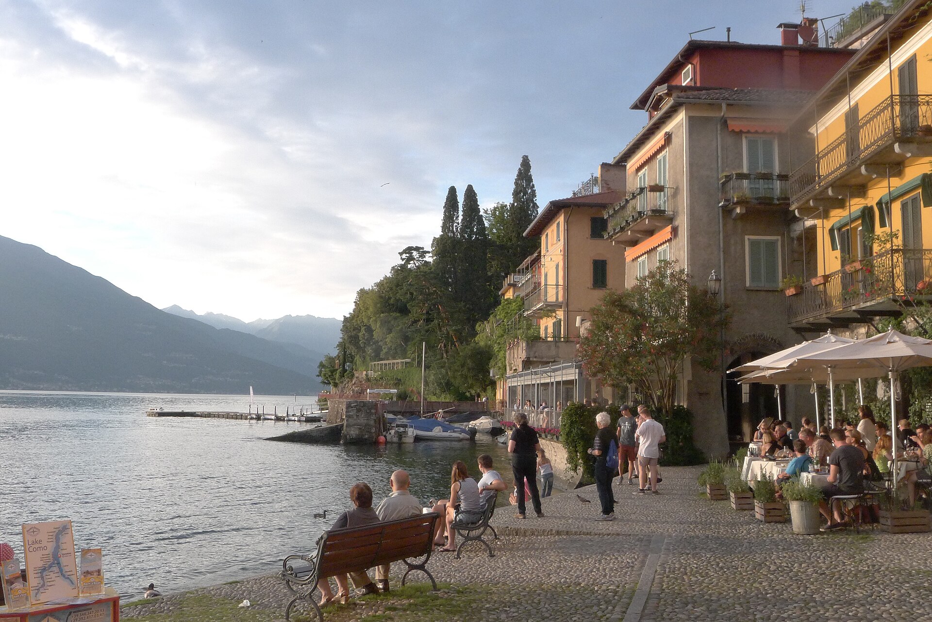 The waterfront of Varenna on the eastern shore of Lake Como, with pastel houses stacked above a small harbor and boats on the water.