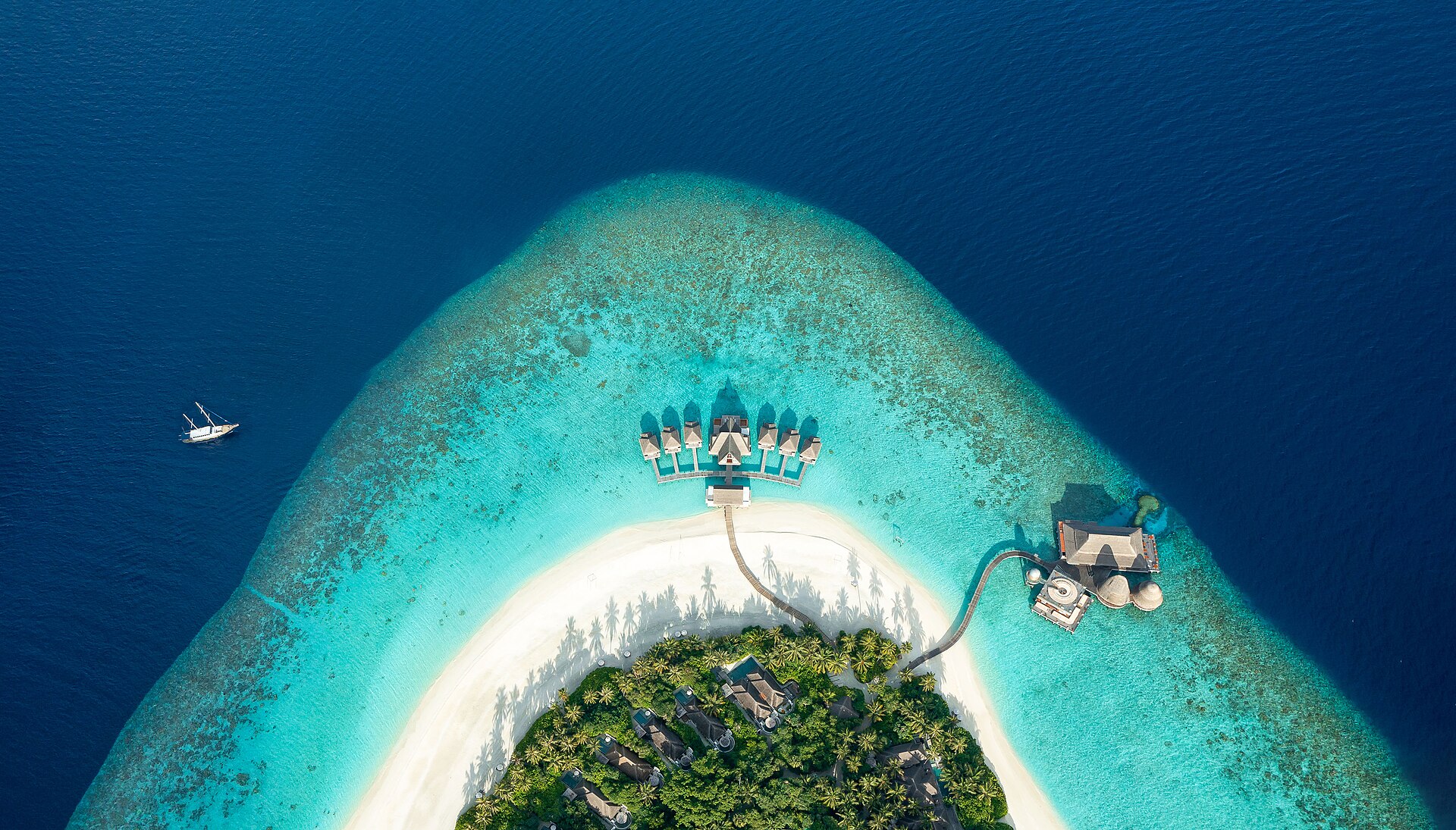 An overwater villa on stilts with a wooden deck and steps leading down into a clear lagoon