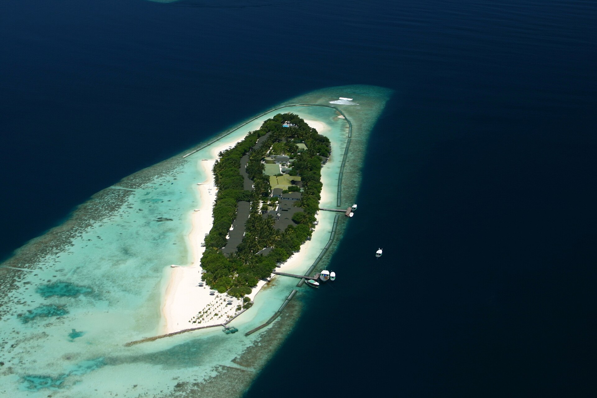 Aerial view of a Maldives resort island ringed by overwater villas and a turquoise lagoon
