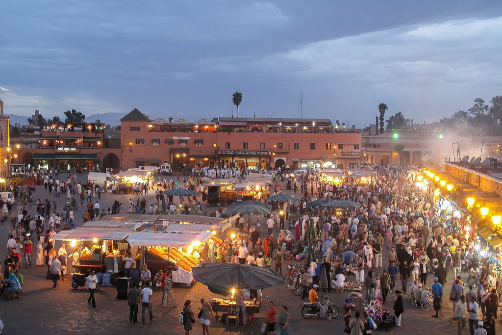 The square Jemaa el-Fnaa in Marrakech at dusk, with the Koutoubia minaret rising behind the crowds and food stalls
