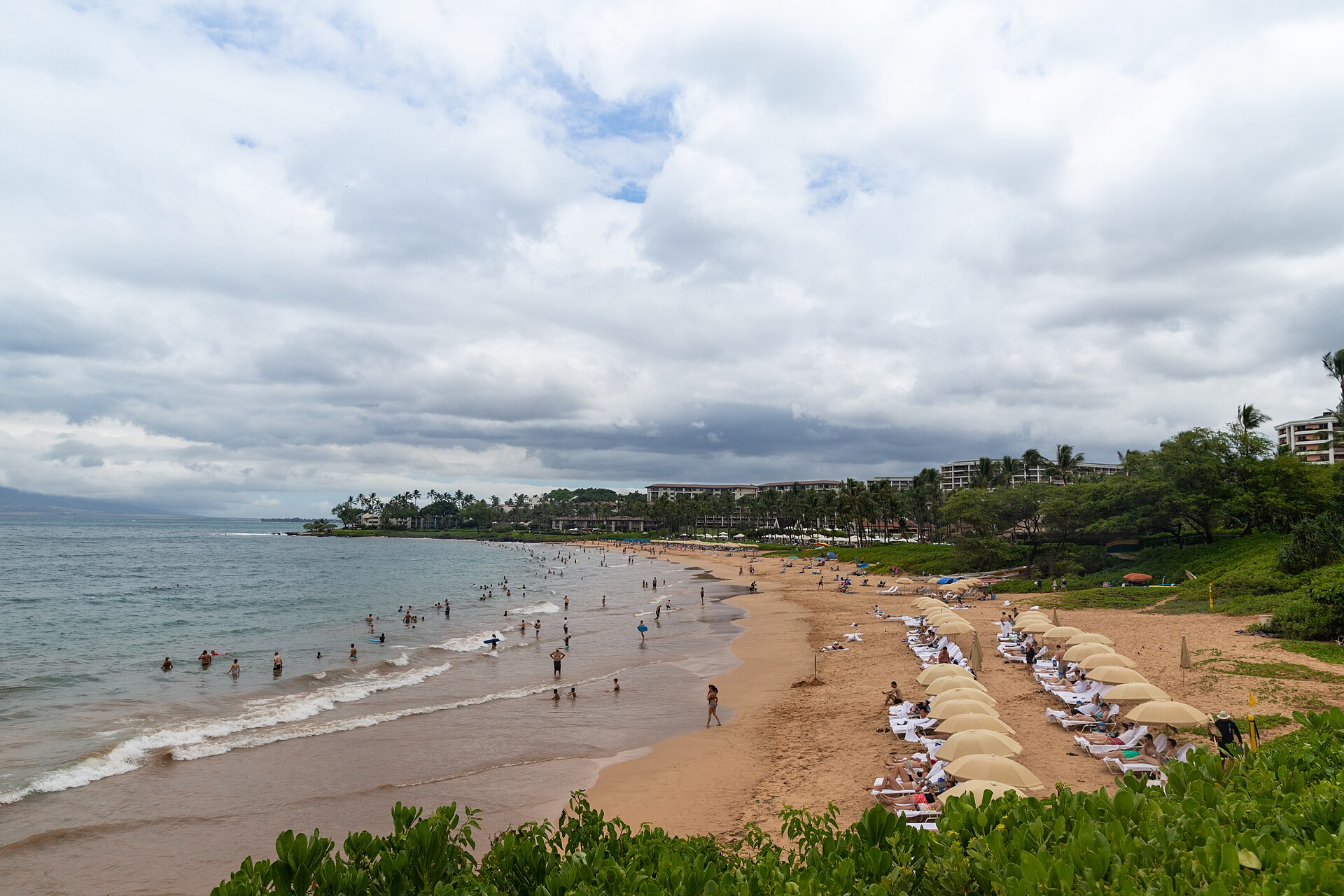 A calm, groomed crescent beach at Wailea on the south coast of Maui, with golden sand, palms, and resort grounds behind a gentle shorebreak.