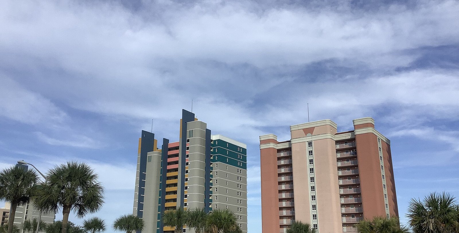 Two high-rise beachfront hotel towers among palmetto palms under a blue sky with large white clouds