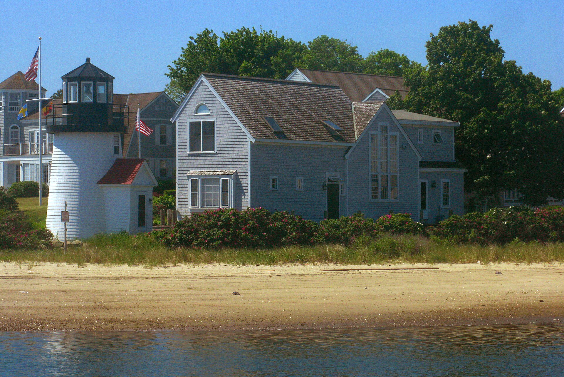 The short white-painted Brant Point Light standing at the sandy entrance to Nantucket harbour with the water behind it.