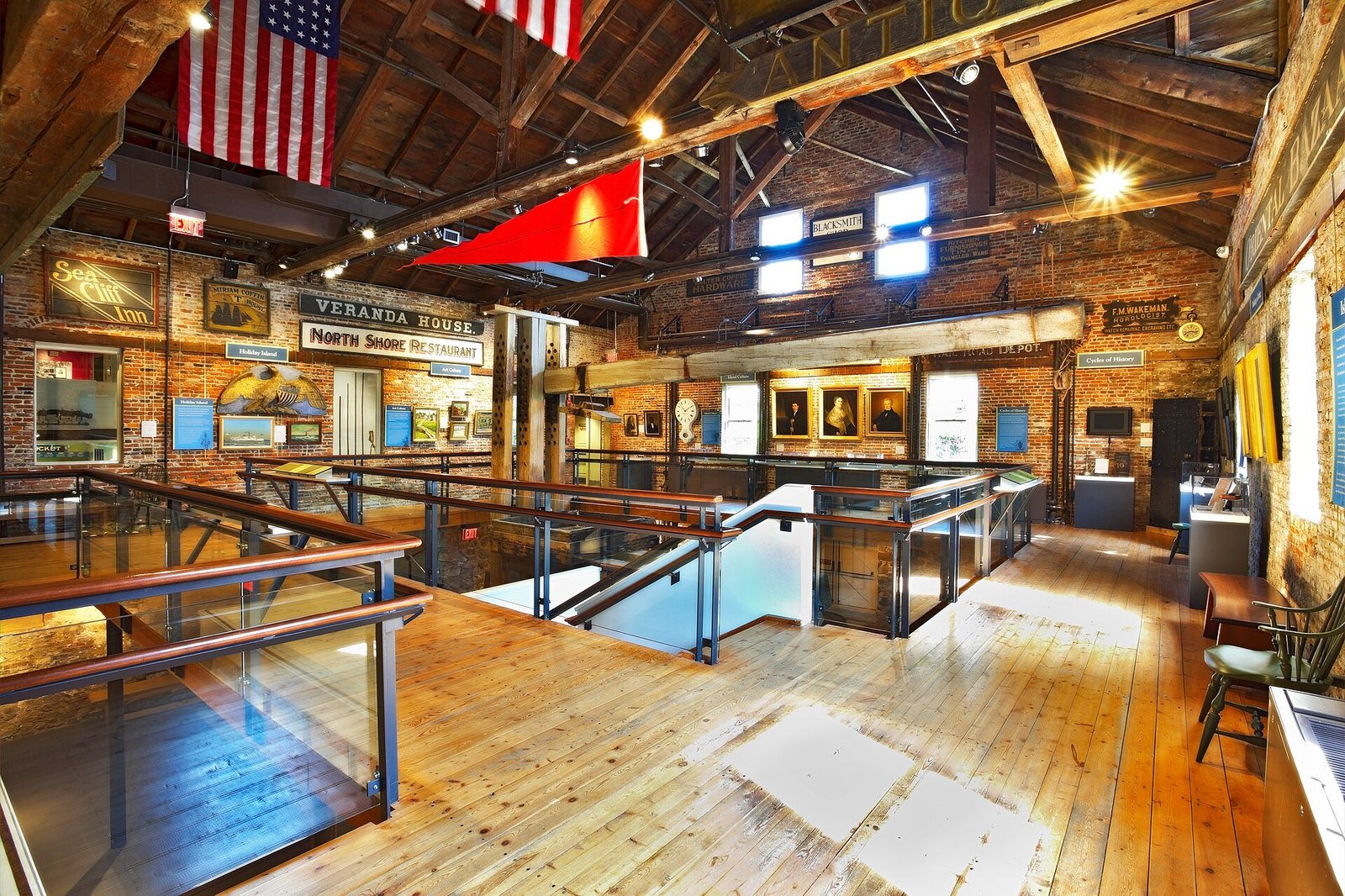 An interior view of a multi-level space with brick walls, wooden floors, exposed ceiling beams, display cases, framed art, and an American flag.