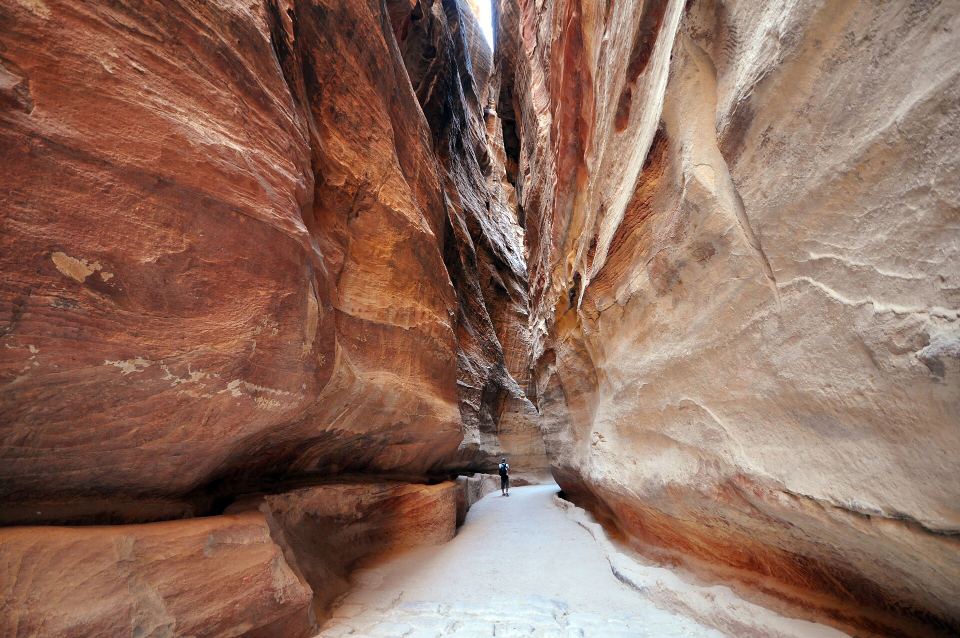A narrow, high-walled sandstone gorge with a paved floor curving between towering striped rock faces.