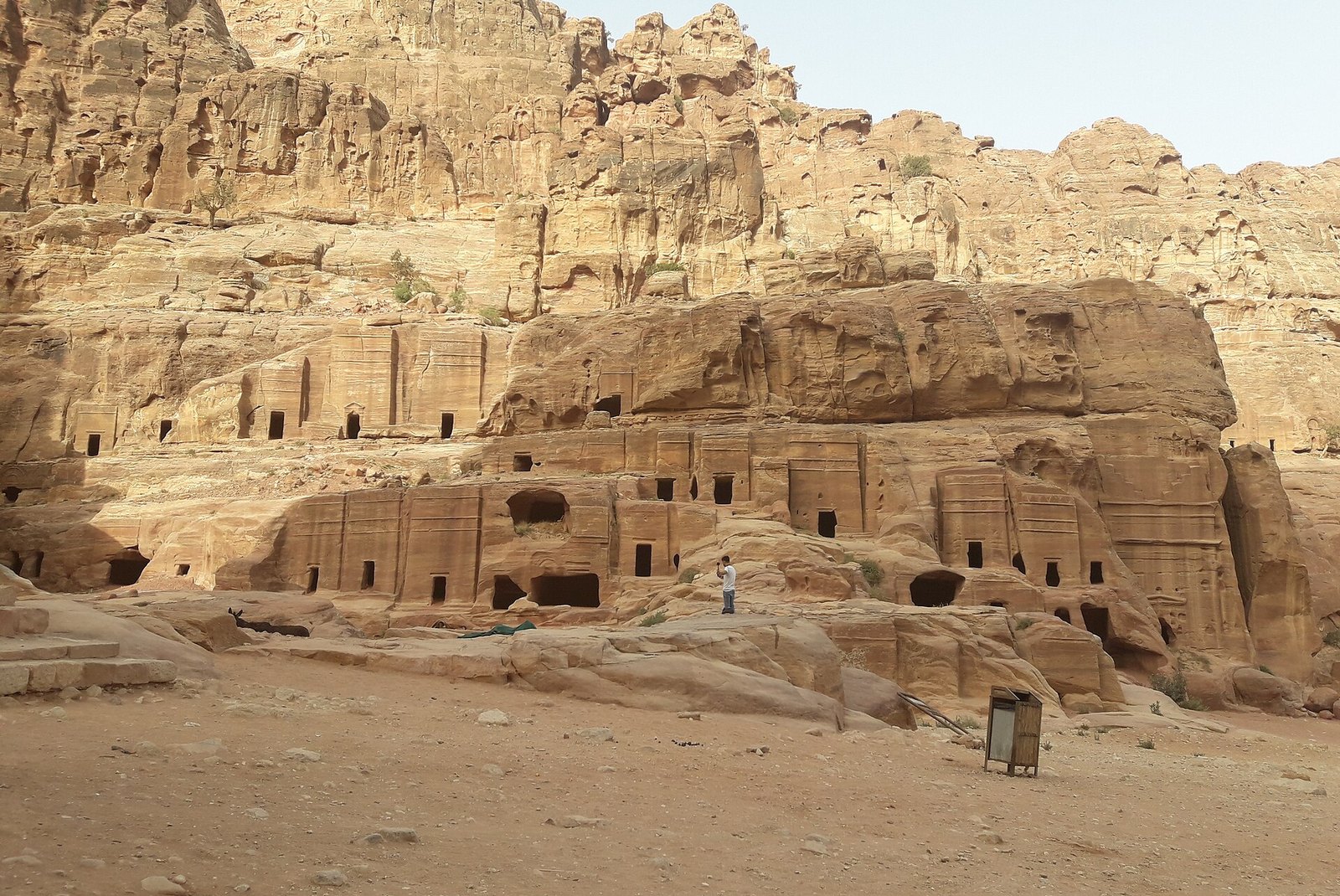 Rock-cut tomb facades with doorways carved into pale sandstone cliffs above a sandy valley floor