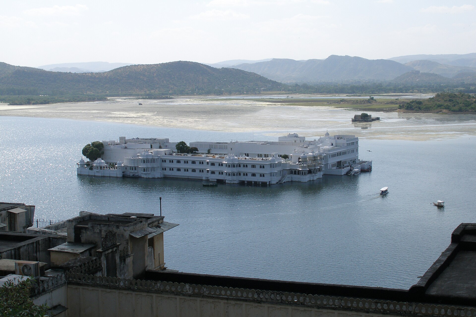 The white marble Taj Lake Palace appearing to float on Lake Pichola, with the hills behind