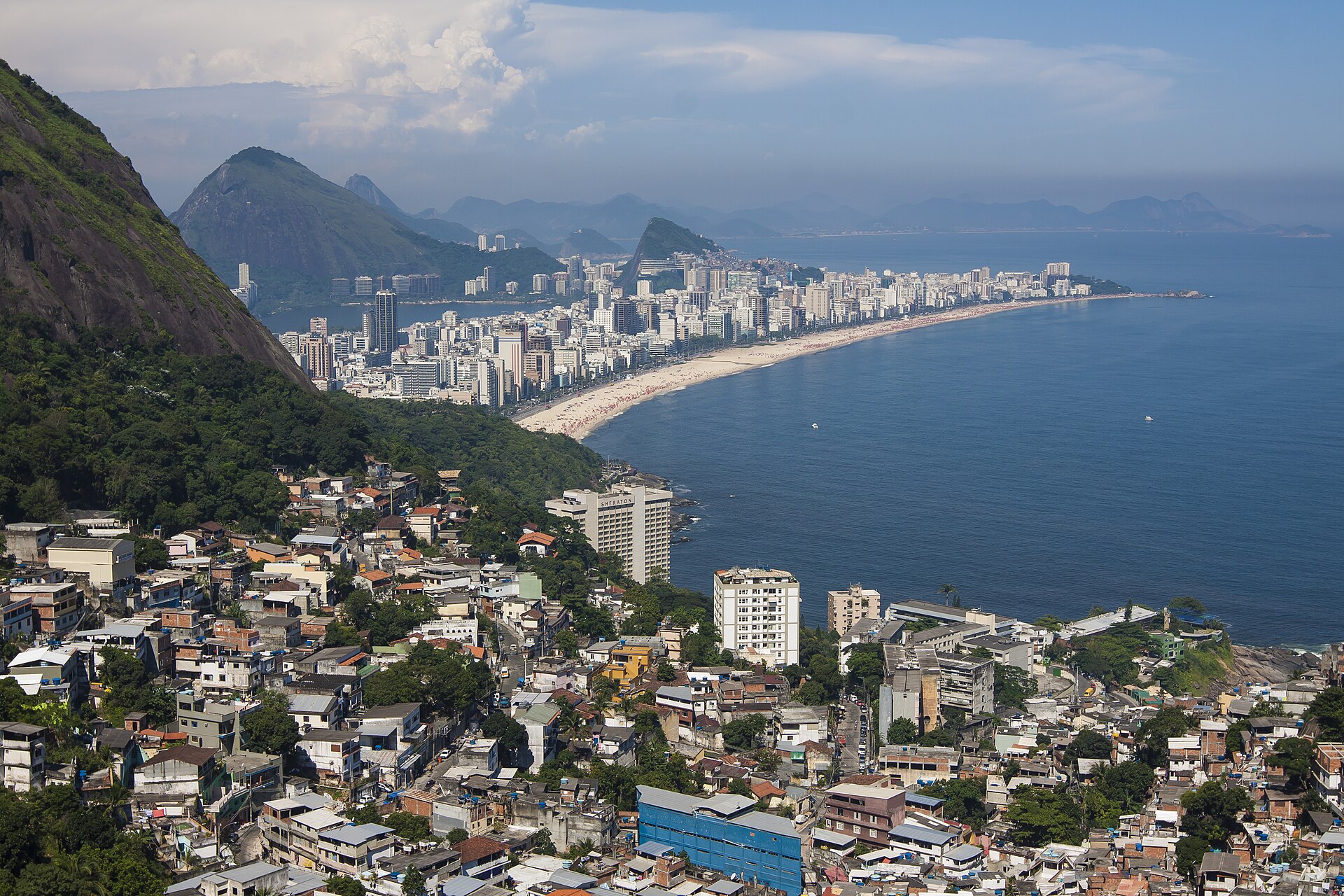 View over Ipanema and Leblon beaches in Rio de Janeiro from a hillside, with a community in the foreground and the peaks of Dois Irmãos and Pedra da Gávea beyond.