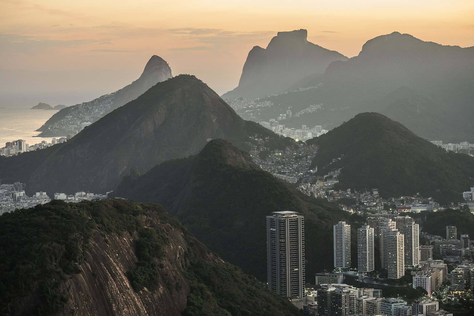 The Zona Sul of Rio de Janeiro seen from Sugarloaf at dusk, with the twin peaks of Dois Irmãos and the rock of Pedra da Gávea rising beyond the beaches and hillside neighbourhoods.
