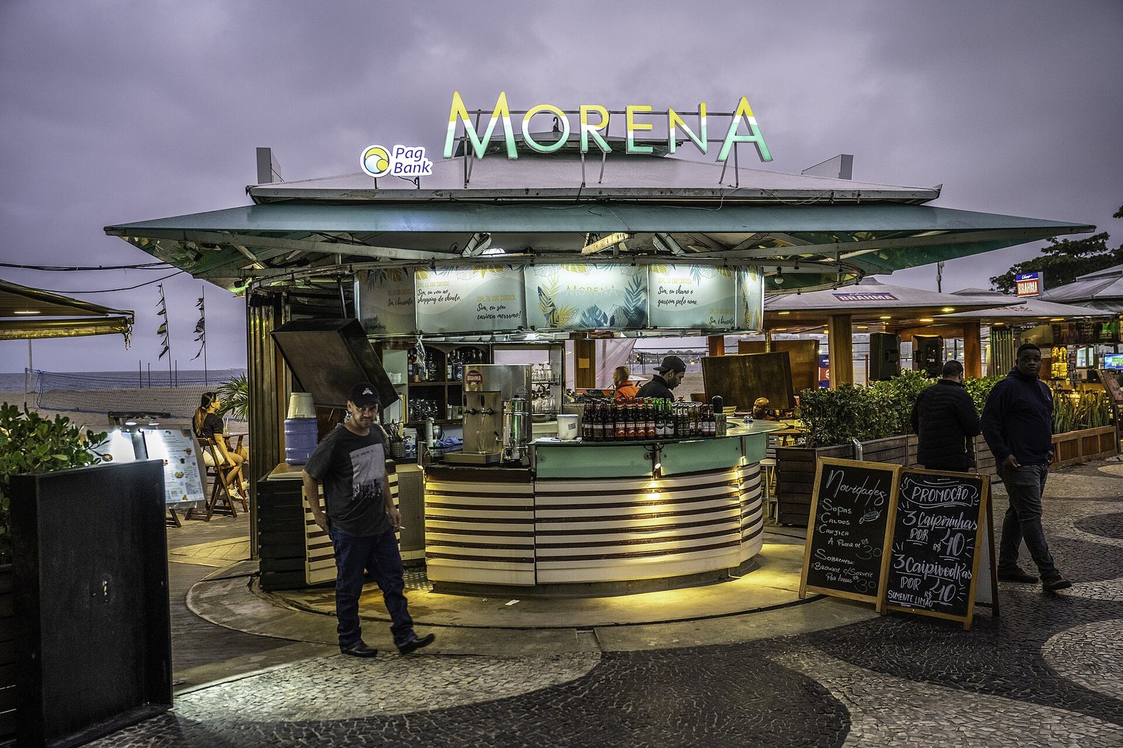 The Morena kiosk on the Copacabana promenade at dusk, lit up beside the patterned pavement.