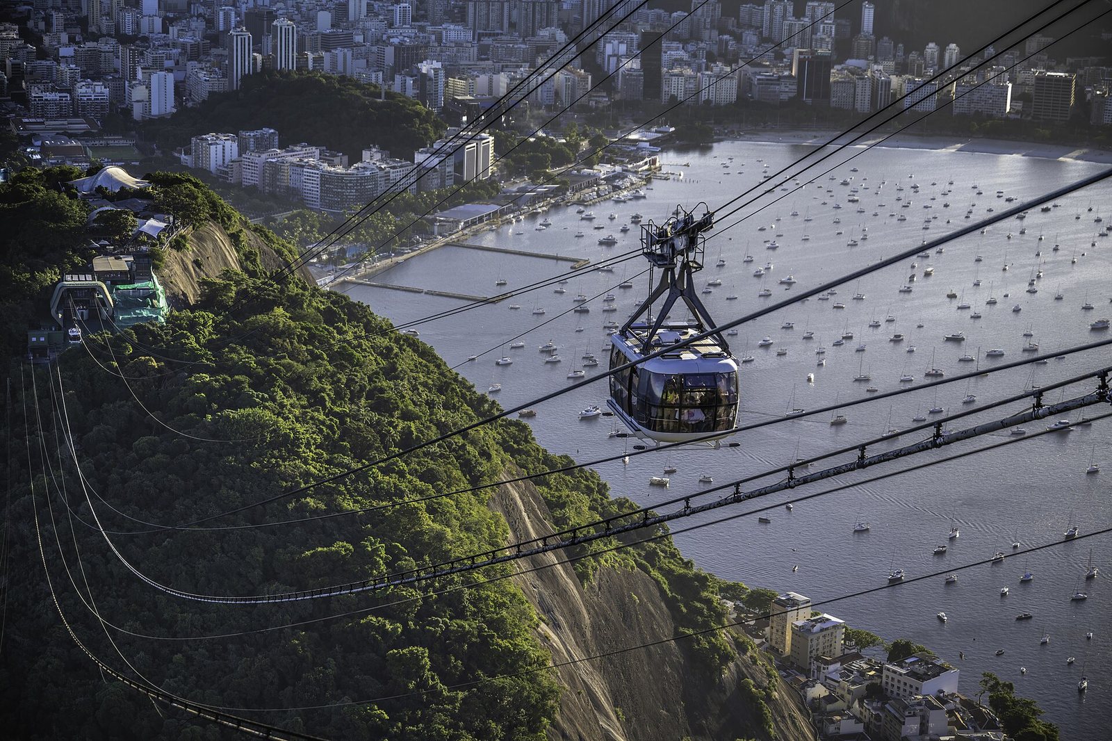 A Sugarloaf cable car crossing above a bay full of moored boats, with the city of Rio behind.