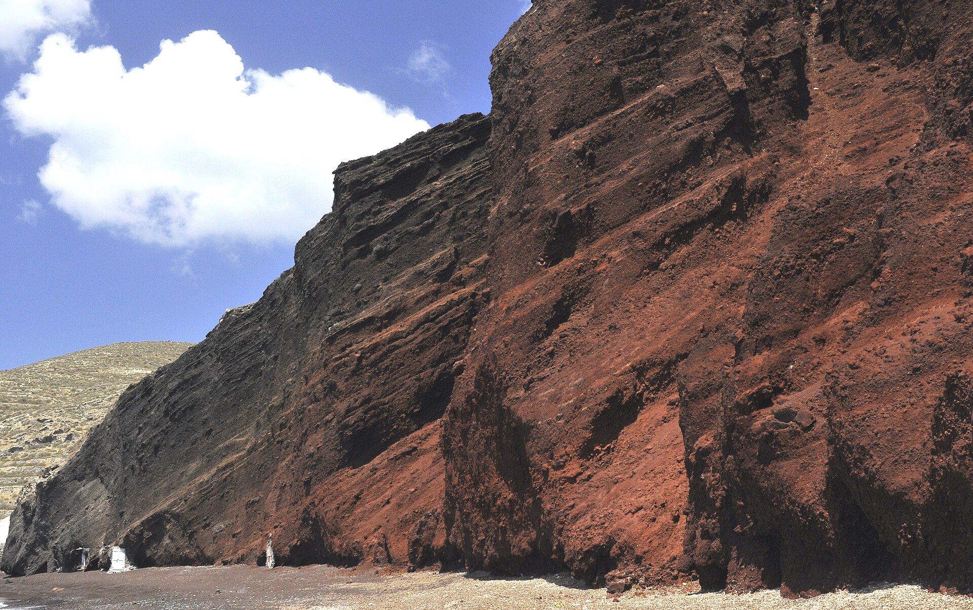 Red volcanic cliffs above a small beach of red and black pebbles at Akrotiri