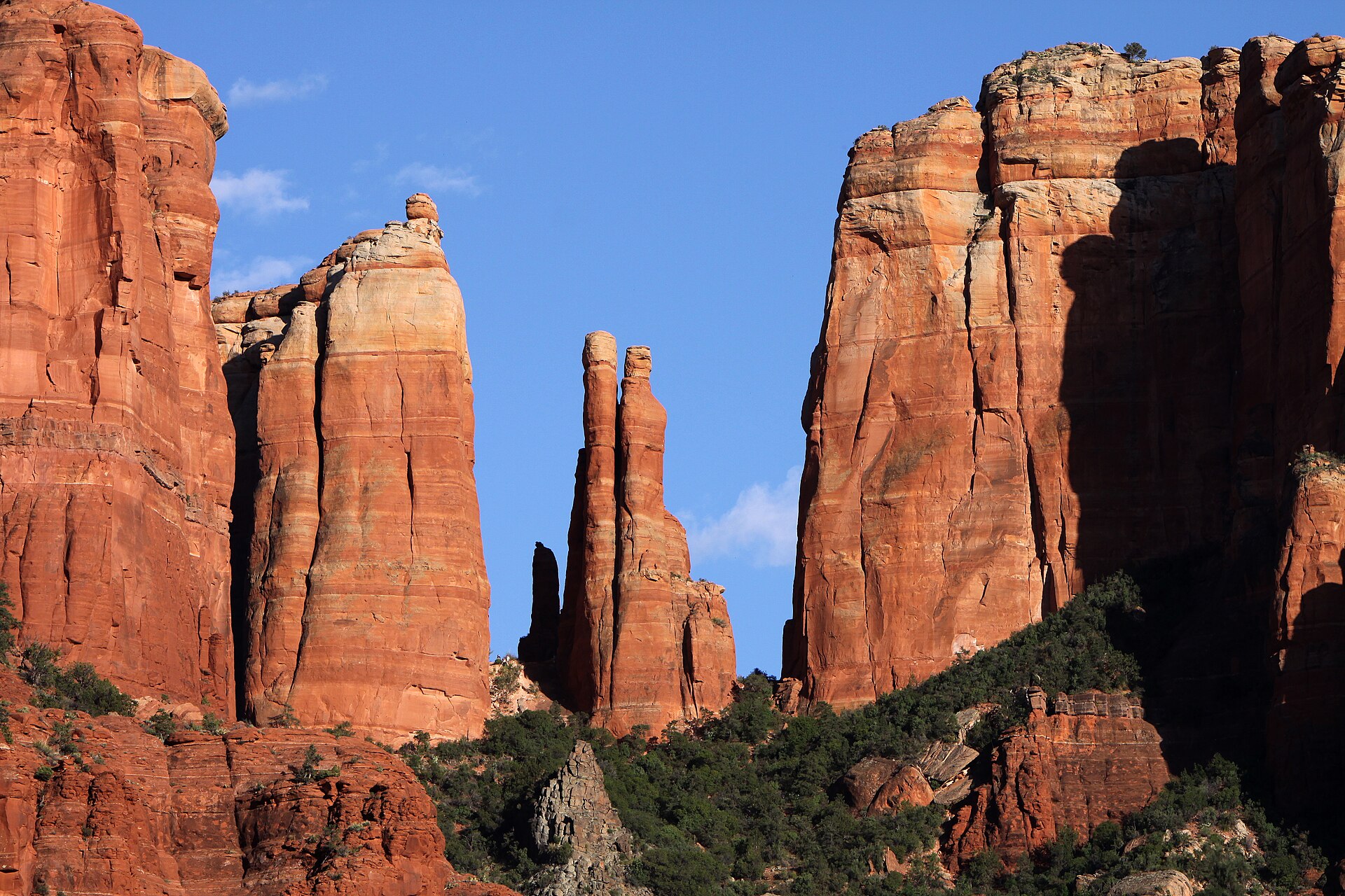 Cathedral Rock in Sedona, Arizona, its red sandstone spires rising above green trees along Oak Creek under a clear sky.