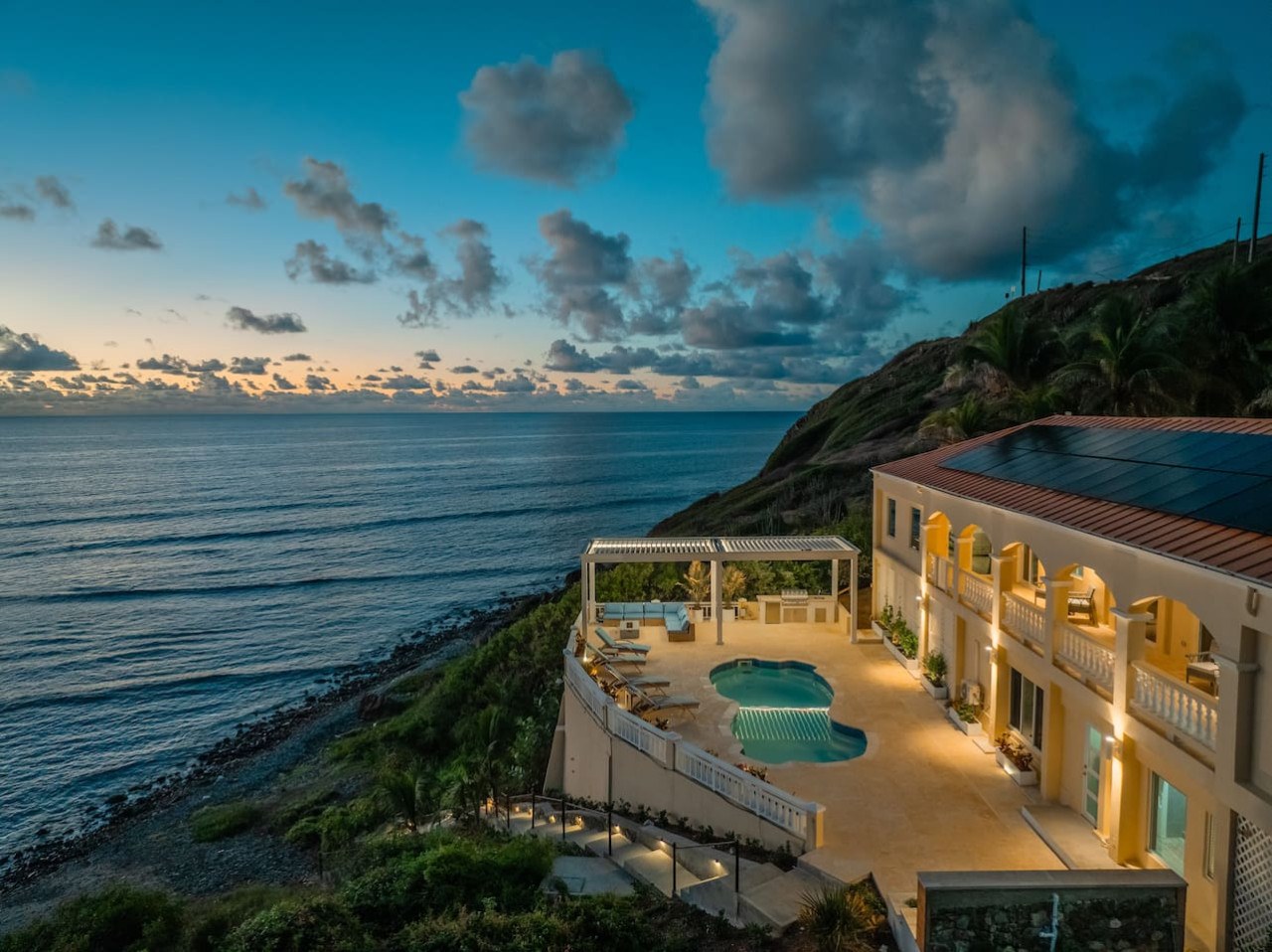 The Cerulean villa at dusk on the slope above the East End shoreline of St. Croix, with its lit pool deck, pergola and arched verandas.