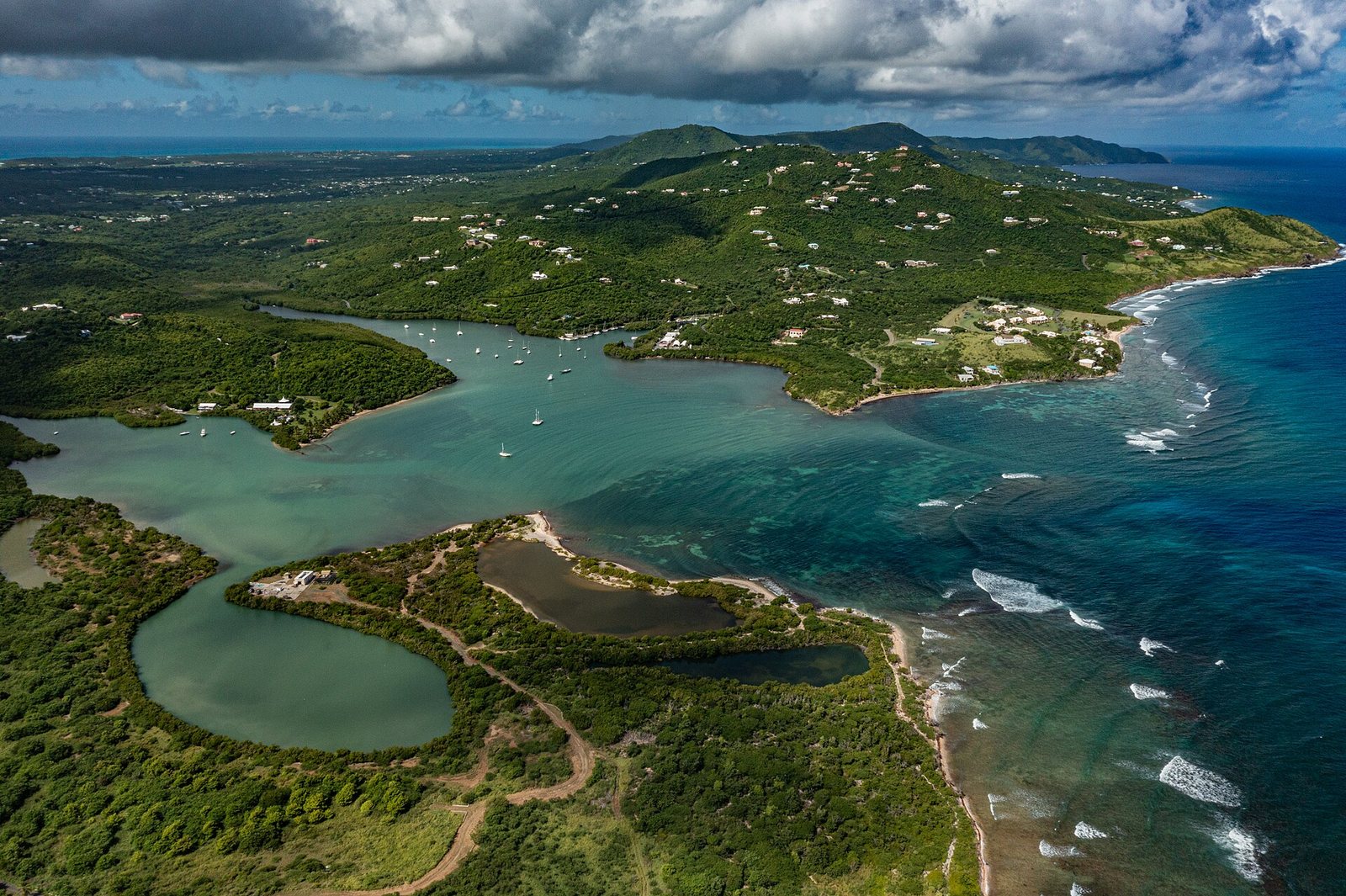 Salt River Bay on the north shore of St. Croix seen from the air, with mangrove-lined water, an inner lagoon, the reef line offshore and green hills behind.