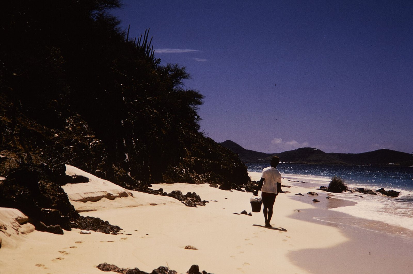 A visitor walking along a beach at Buck Island Reef National Monument, with the sea and hills in the distance.