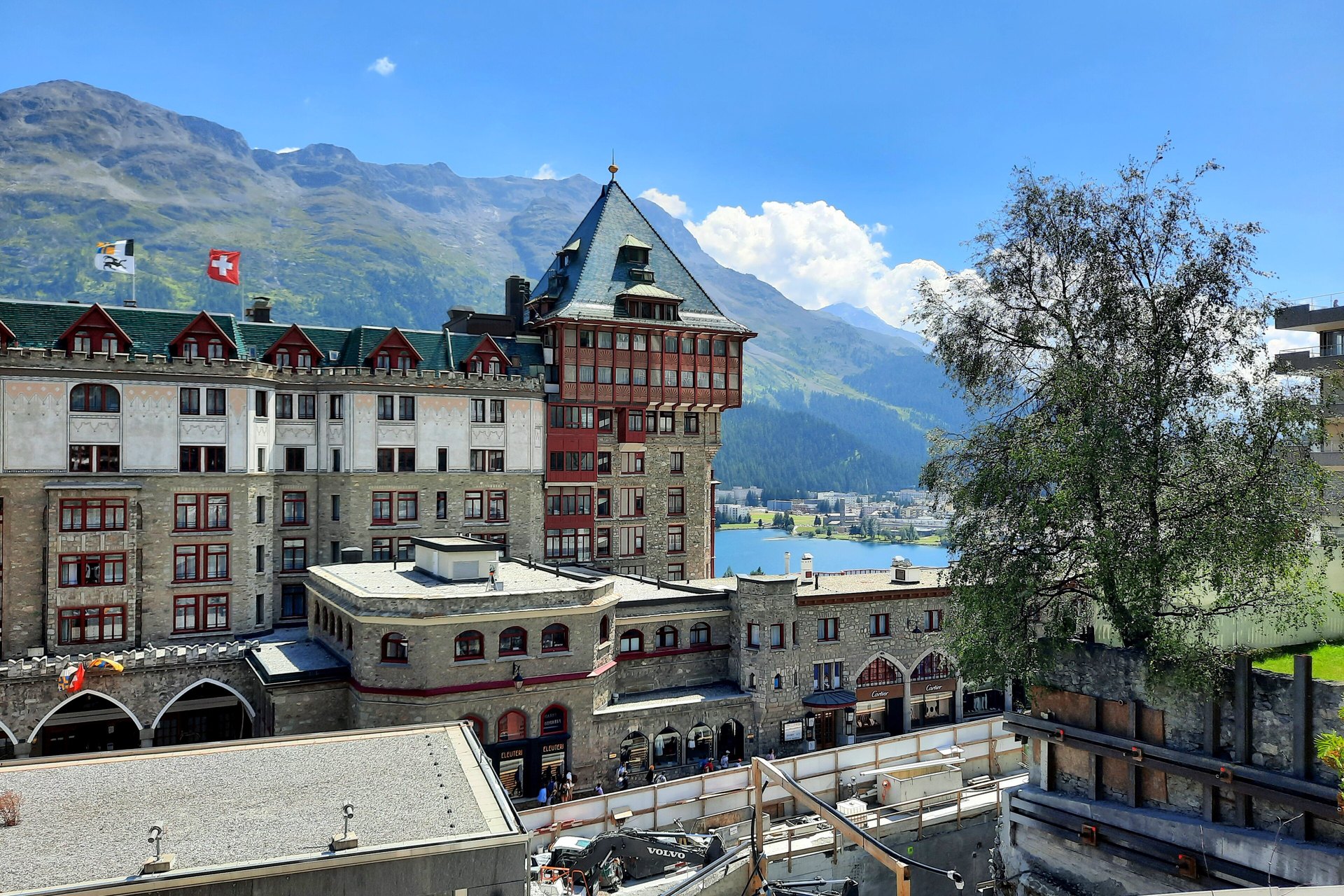 The tower and facade of Badrutt’s Palace Hotel above the town of St. Moritz, with mountains and the lake behind